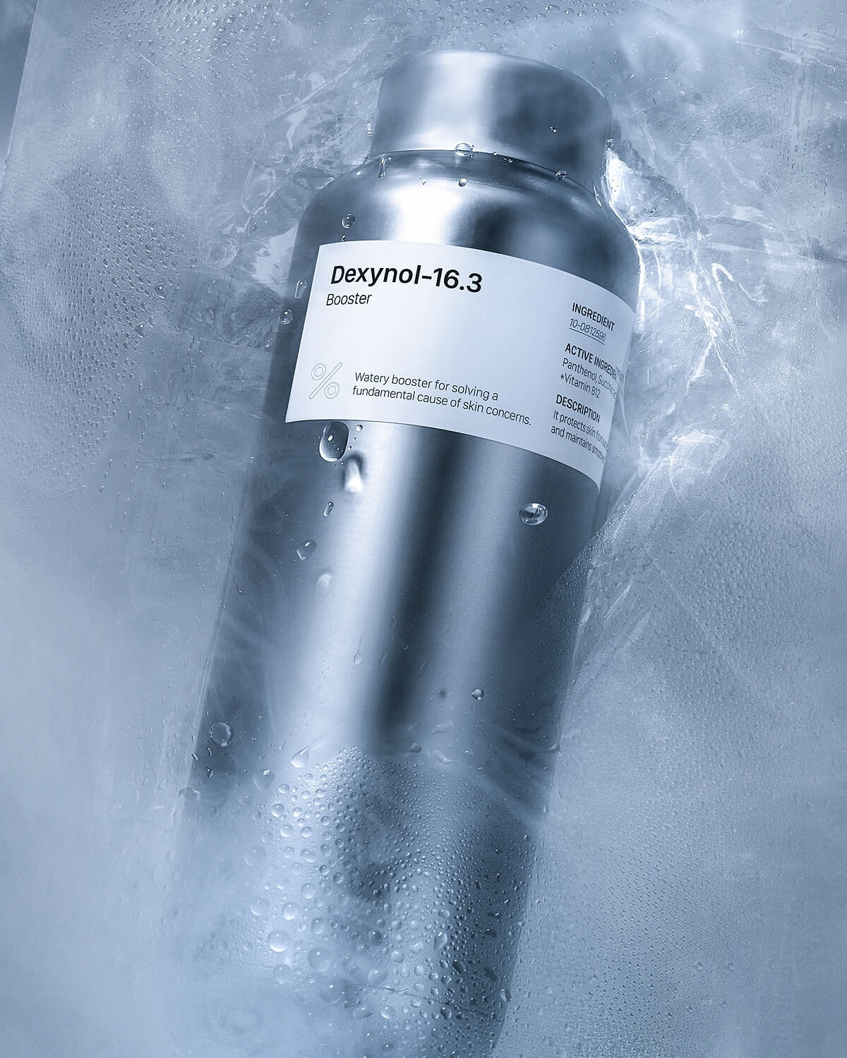 Close-up of the Percent Science Dexynol-16.3 Booster Essence in a silver metallic bottle, covered in condensation/water droplets, highlighting the label that mentions it is a 'Watery booster' and lists active ingredients.