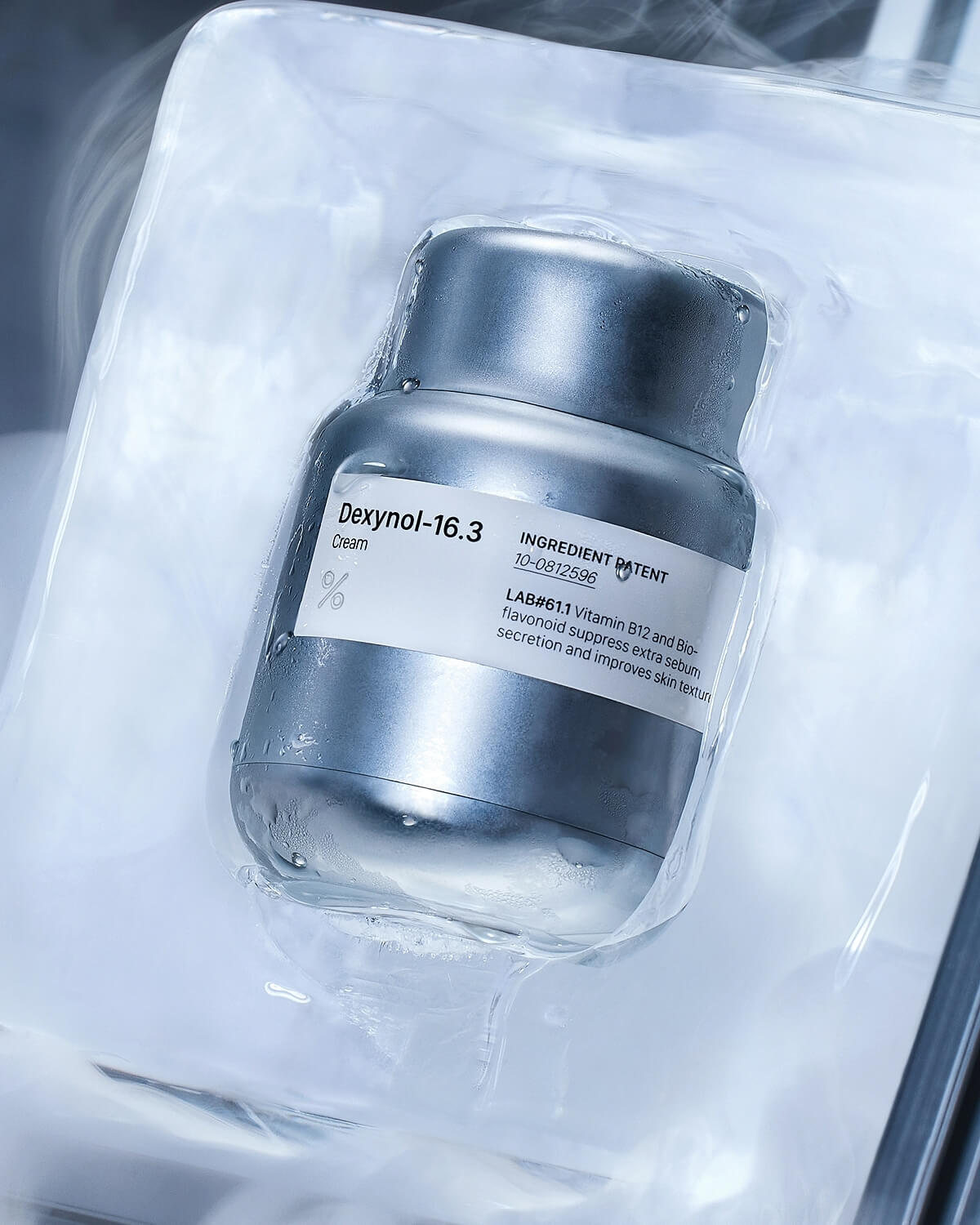 The Dexynol-16.3 Cream silver jar is shown inside its transparent, plastic-like packaging, with condensation and a frosted, icy effect.