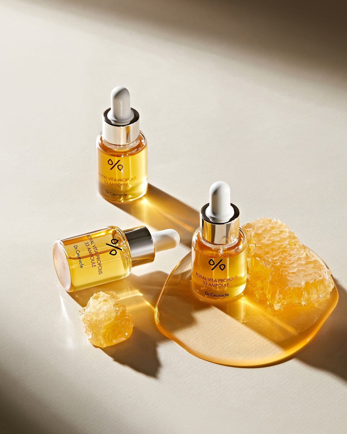 Three bottles of Dr. Ceuracle Royal Vita Propolis 33 Ampoule with honeycomb and honey drops, showing the serum's golden color.