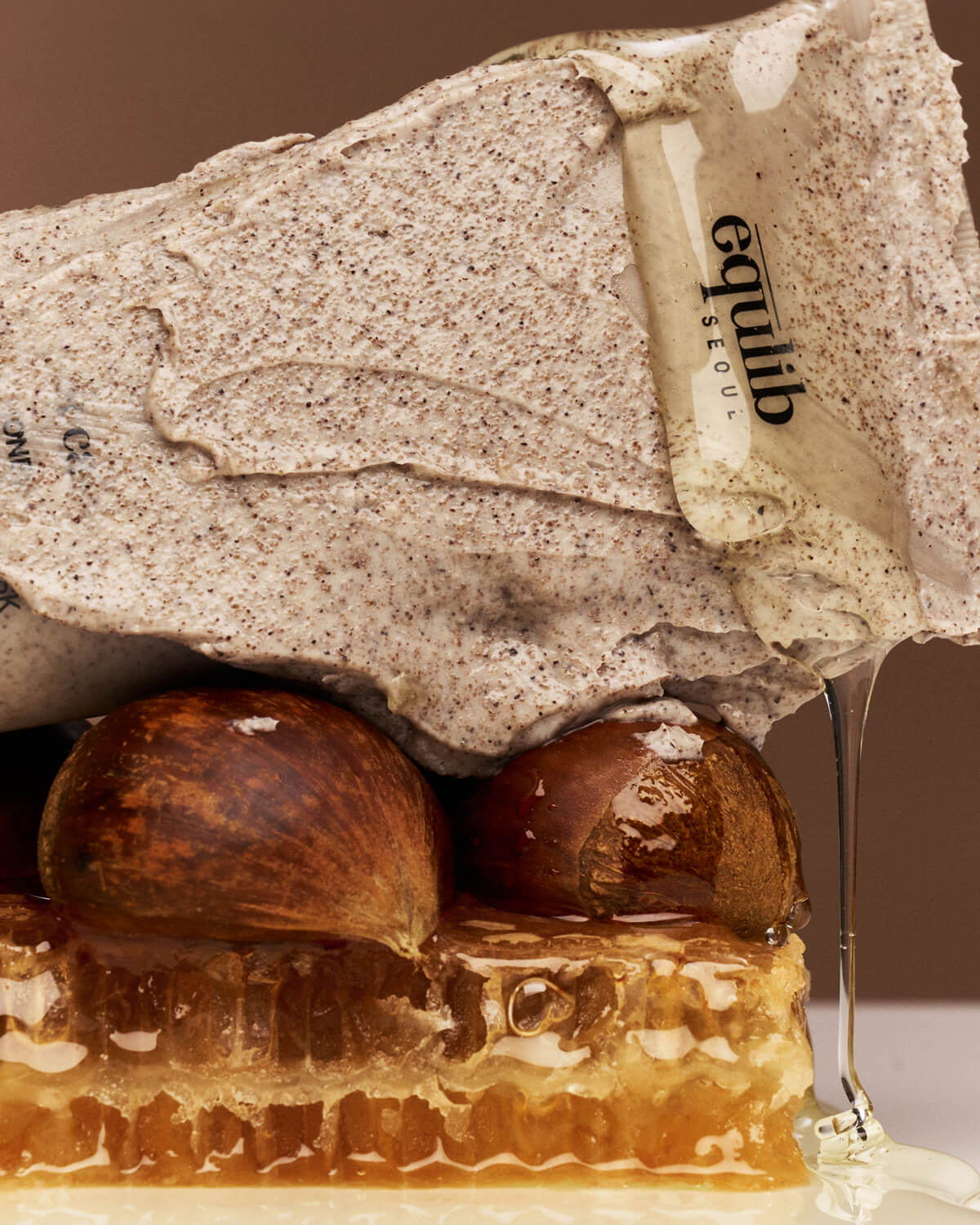 Close-up of Equlib Eau Calm clay mask texture smeared over whole chestnuts and a dripping honeycomb block.