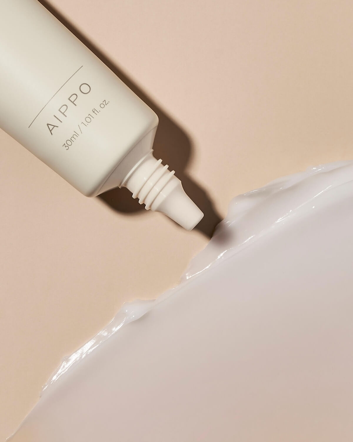 A close-up shot of the tube's nozzle dispensing the thick white cream onto a soft beige surface, where it is spread into a smooth, thick layer.