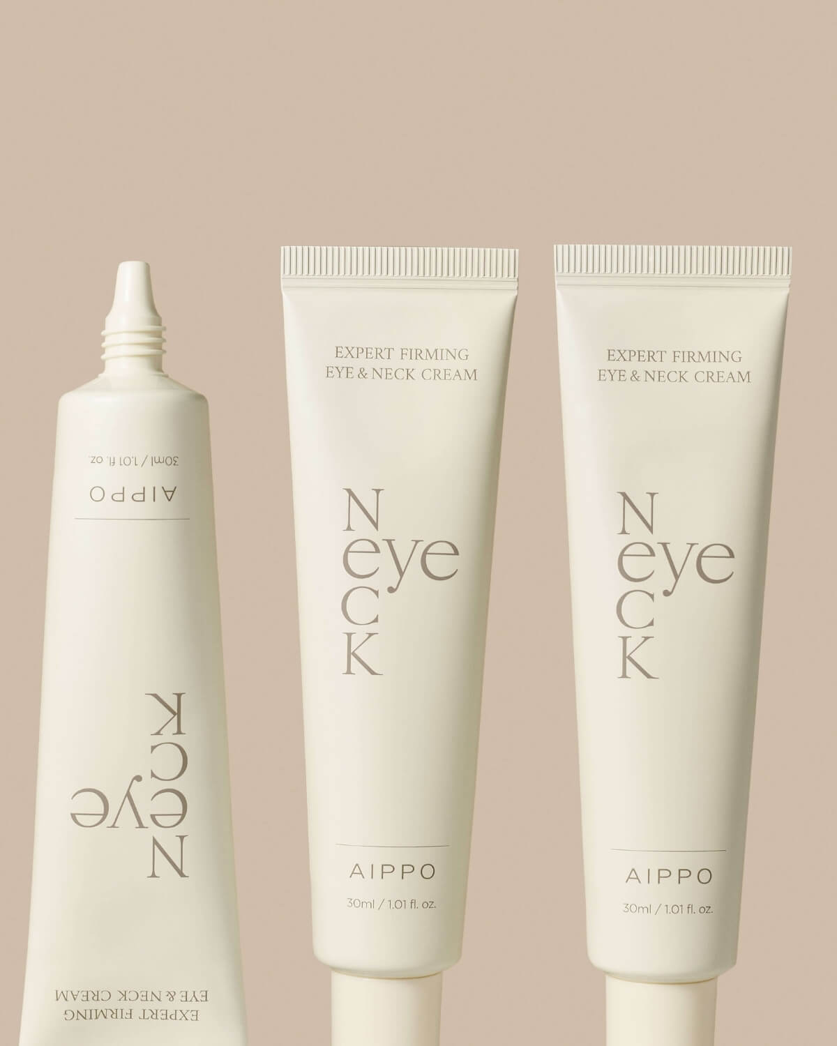 A close-up arrangement of three tubes of the Aippo Expert Firming Eye & Neck Cream against a soft, pale background. One tube is shown with the cap off and nozzle visible on the left, while the other two stand upright.