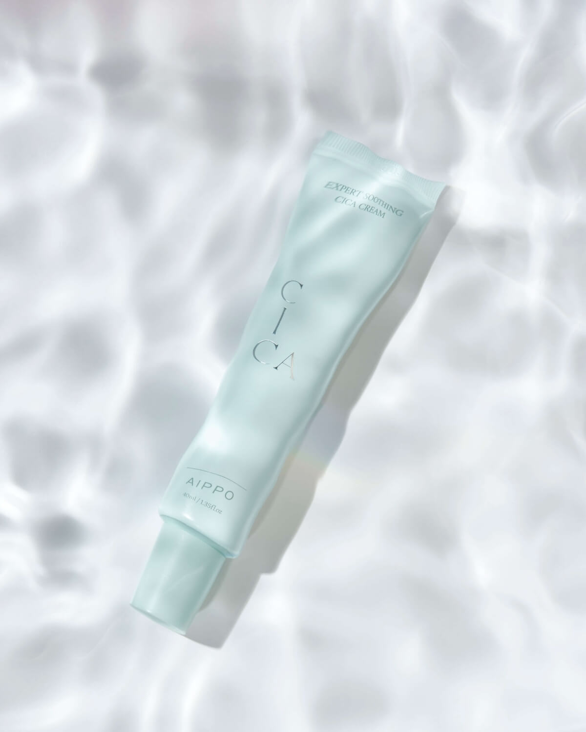 The Cica Cream tube is angled and overlaid with a shimmering, water-like ripple texture, giving the impression of being submerged or reflecting bright light off water.