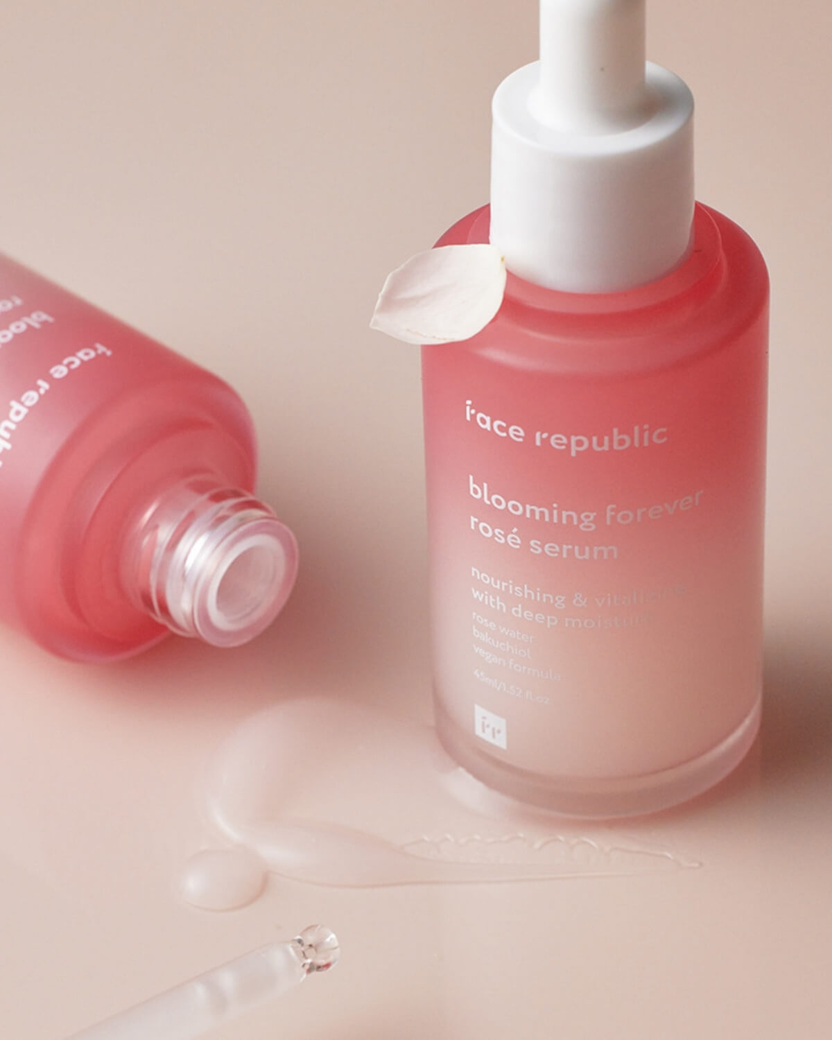 Close-up of pink glass serum bottle with liquid texture and rose petal.