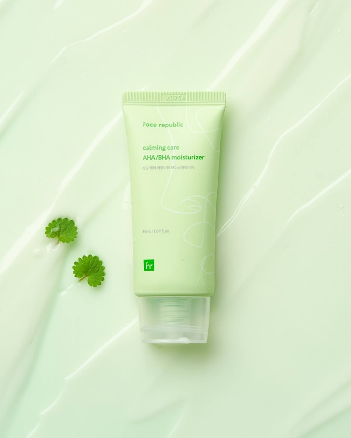 Face Republic Calming Care moisturizer tube lying on a smooth green cream texture with small leaves.