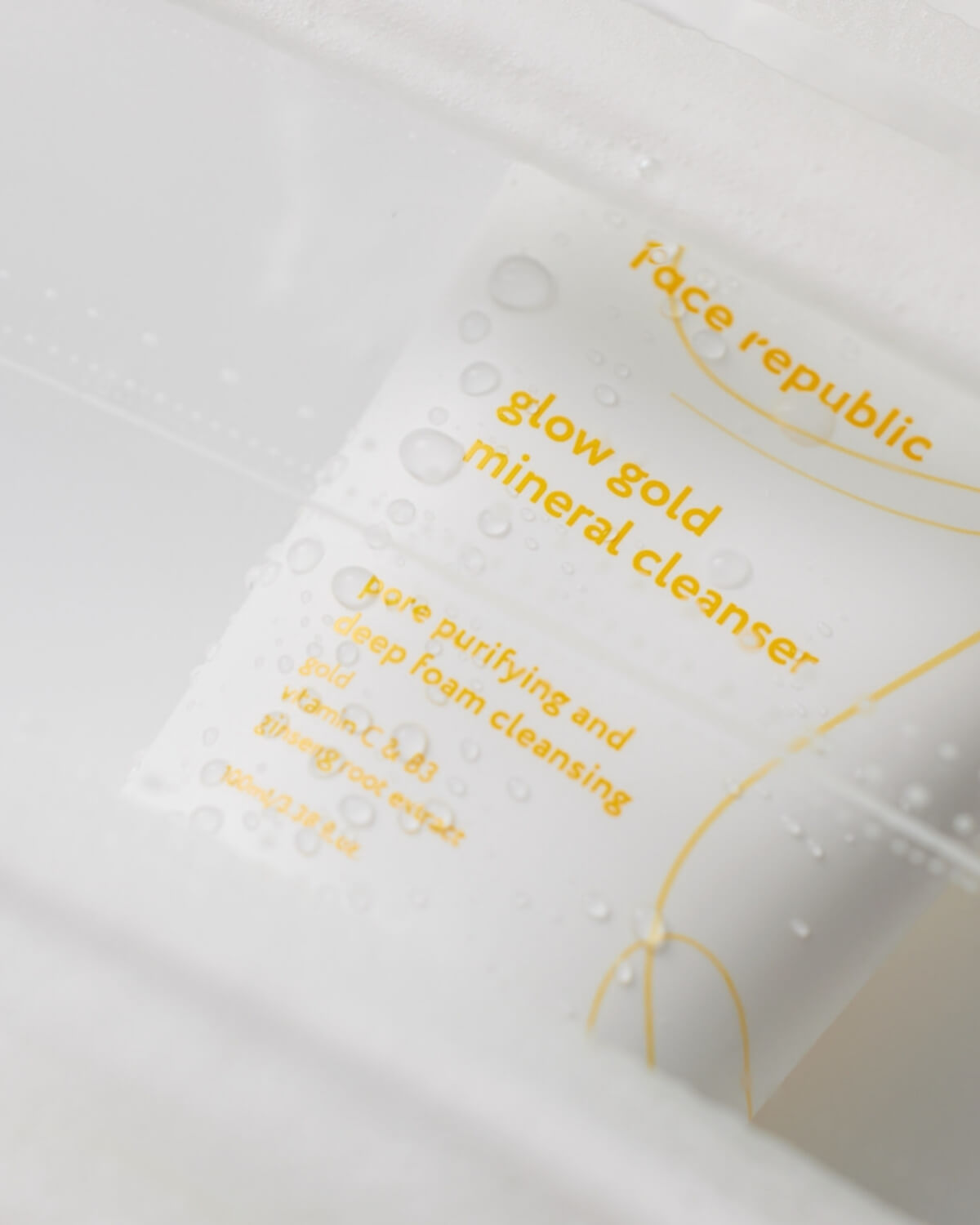 Macro shot of water droplets on the Face Republic Glow Gold Mineral Cleanser tube packaging.