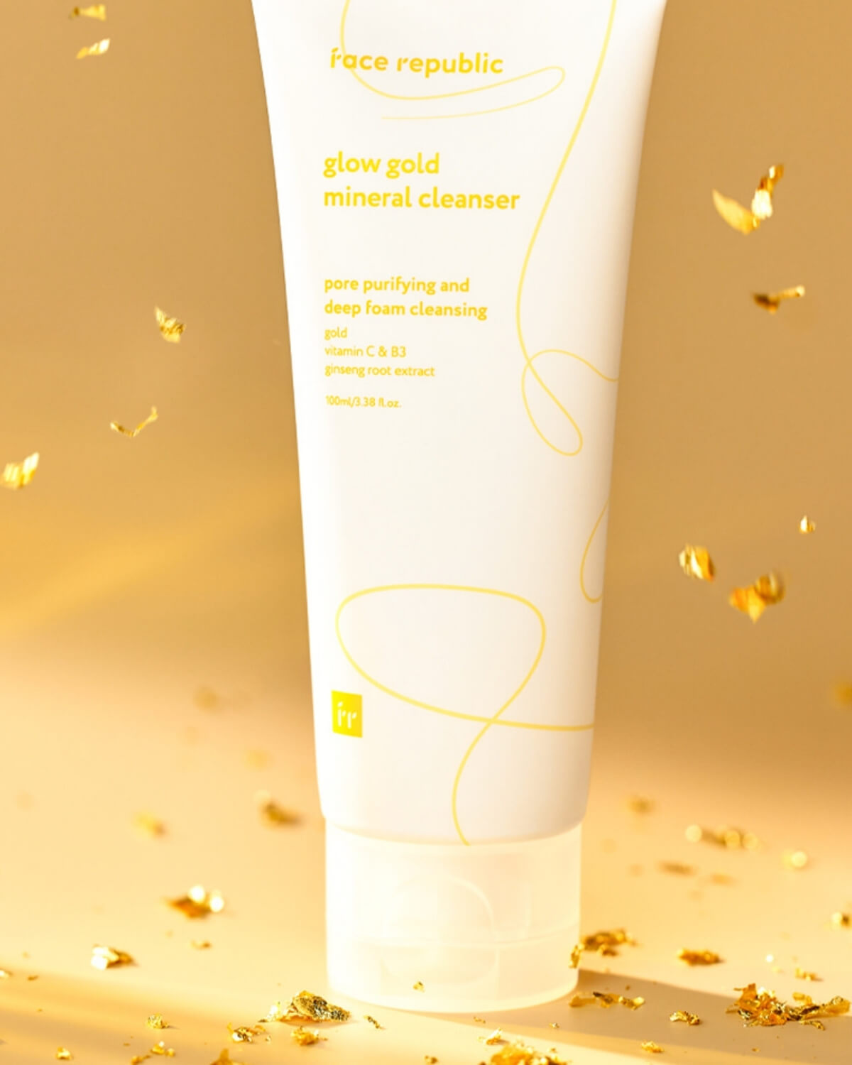 Close-up of Face Republic Glow Gold Mineral Cleanser tube with gold leaf flakes scattered around the base.