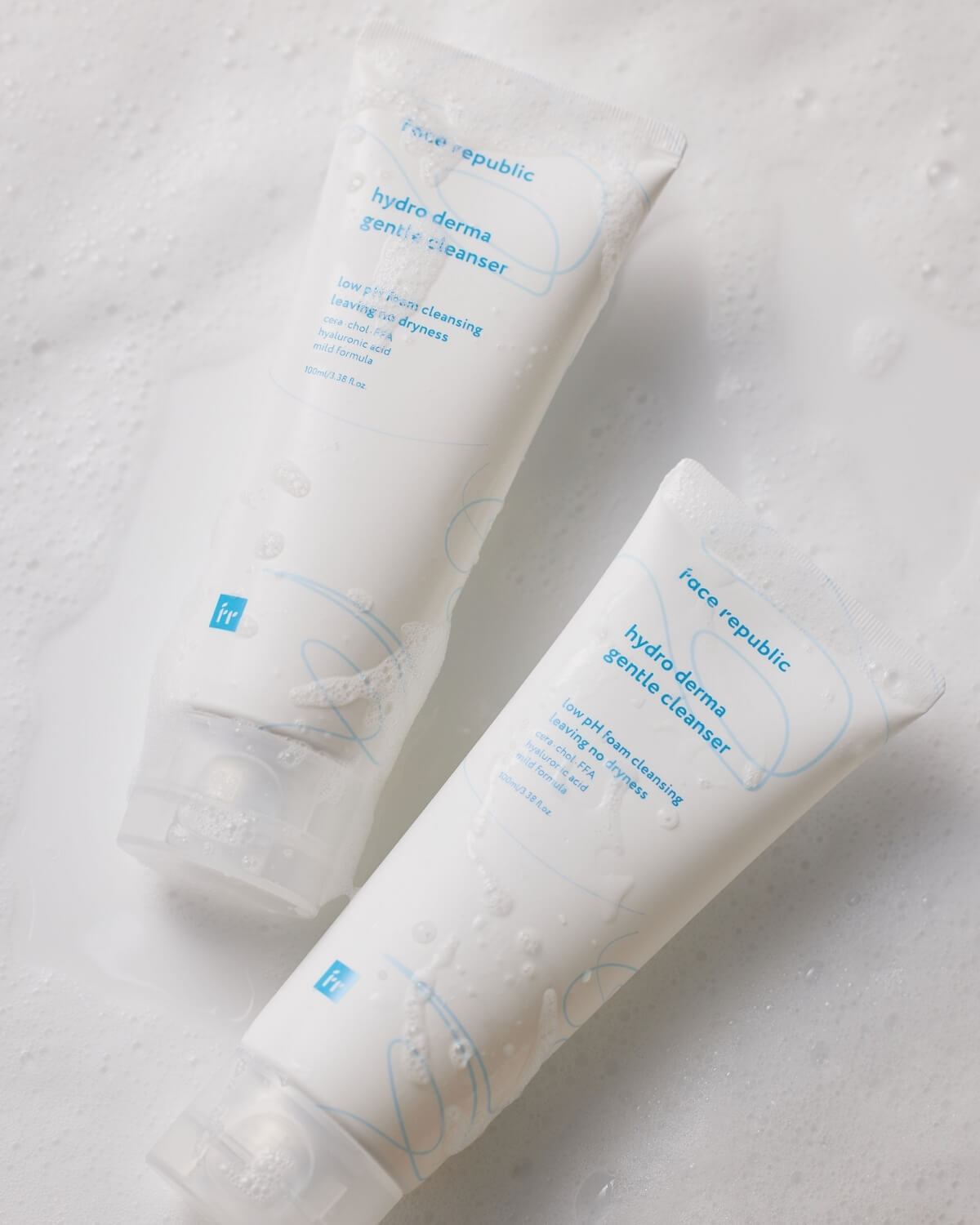 Two tubes of Face Republic Hydro Derma Gentle Cleanser laying on a surface covered in soapy foam.