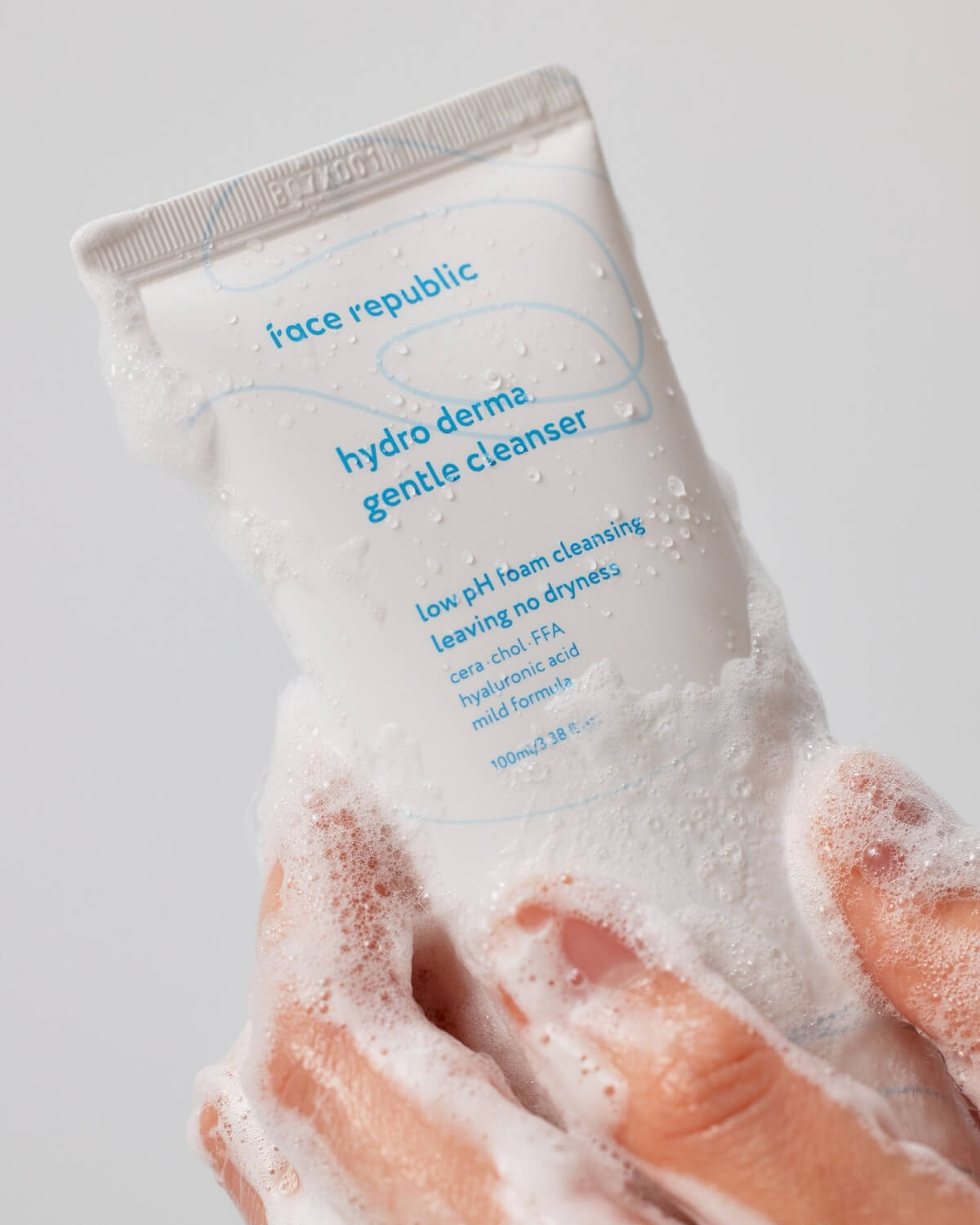 Hands holding the Face Republic Hydro Derma Gentle Cleanser tube covered in rich cleansing foam.