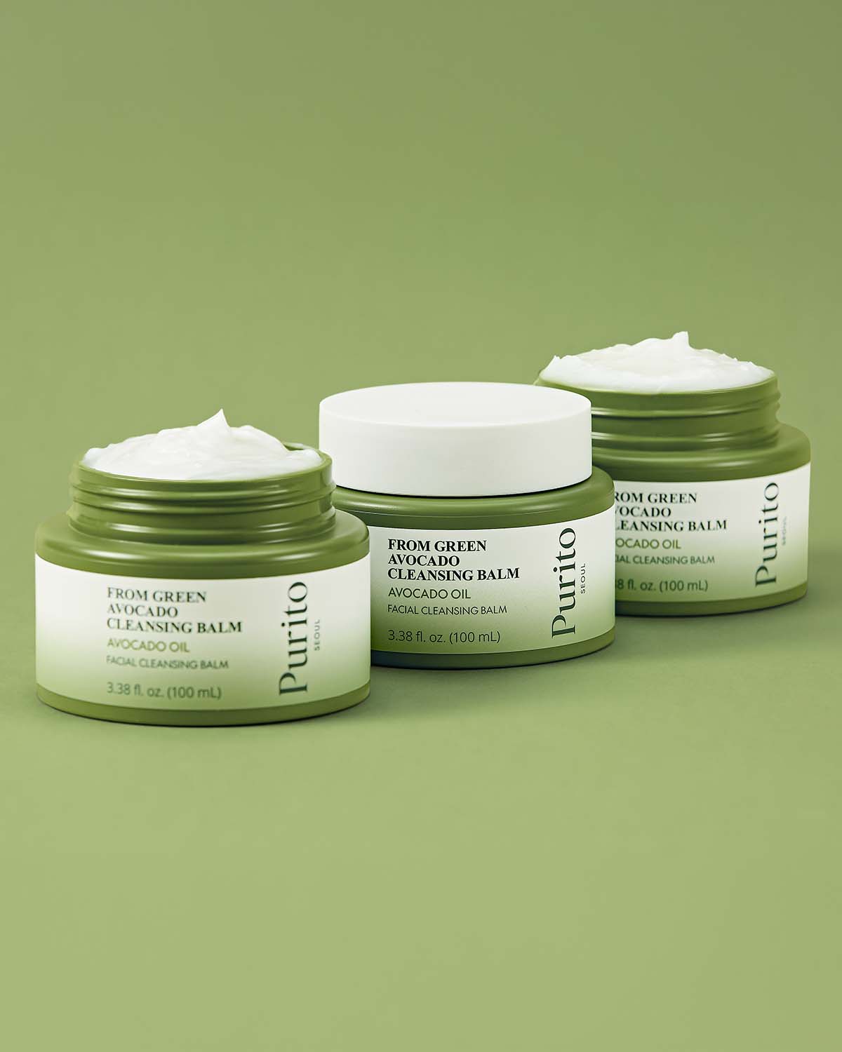 Three jars of Purito Avocado Cleansing Balm on a green background, two open showing the white balm texture.
