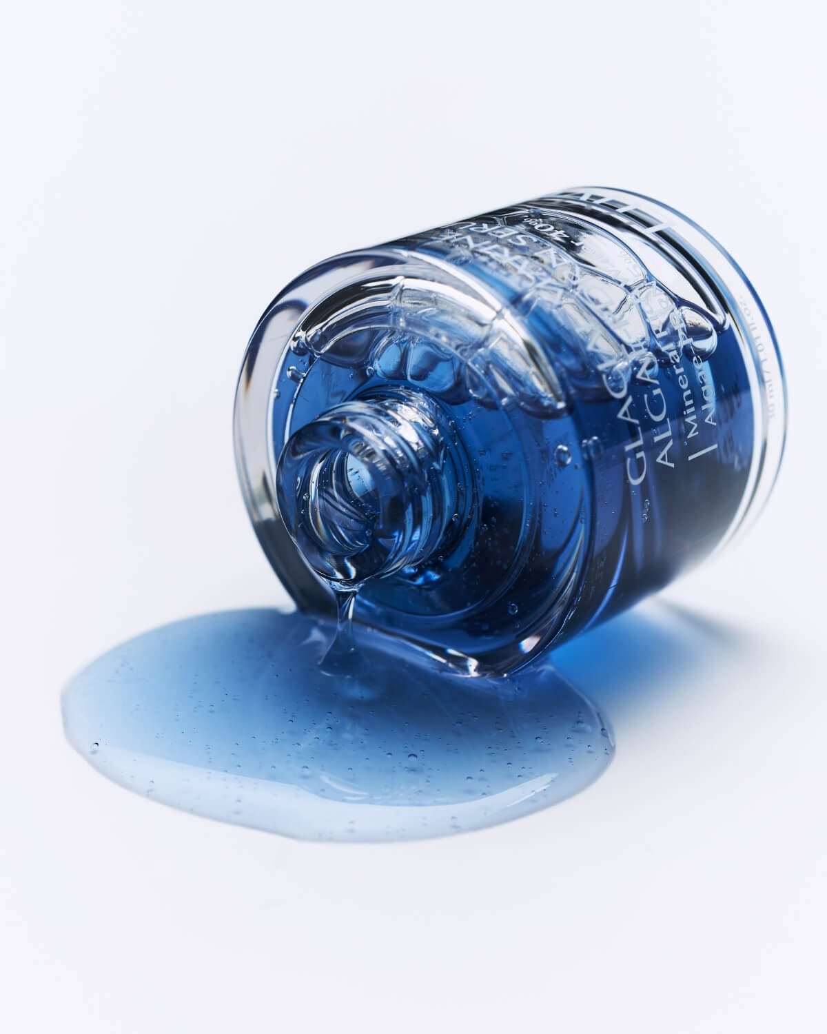 Luvum Glacial Marine Algae-PDRN Serum bottle tilted on its side with blue liquid spilling onto a white surface.
