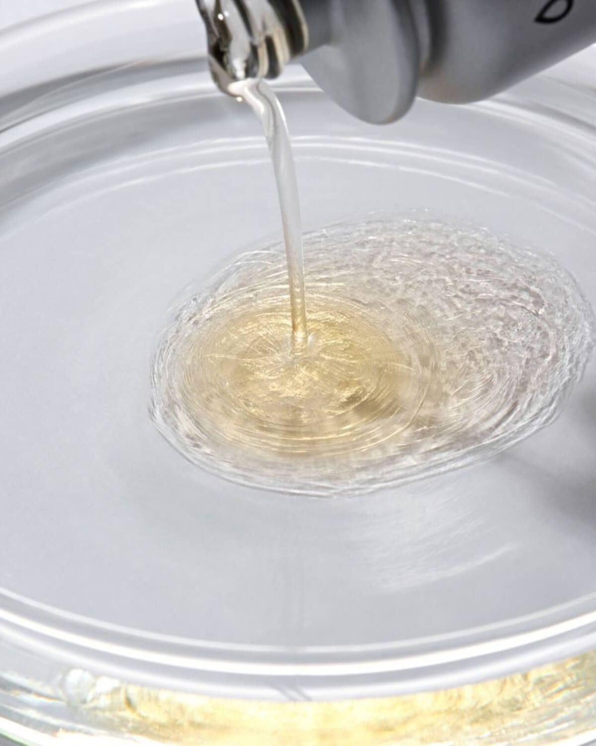 Macro shot of clear Glutathione & NMN serum being poured into a glass lab dish.