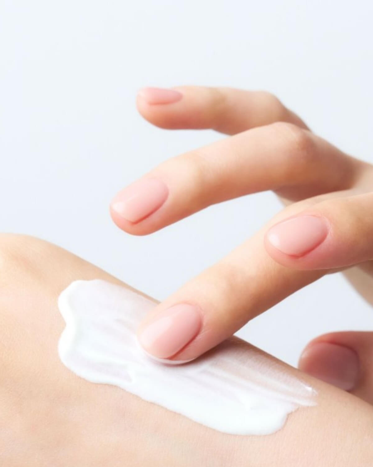 Close-up of a smooth white cream sunscreen texture being gently blended onto skin by fingers with a natural manicure.