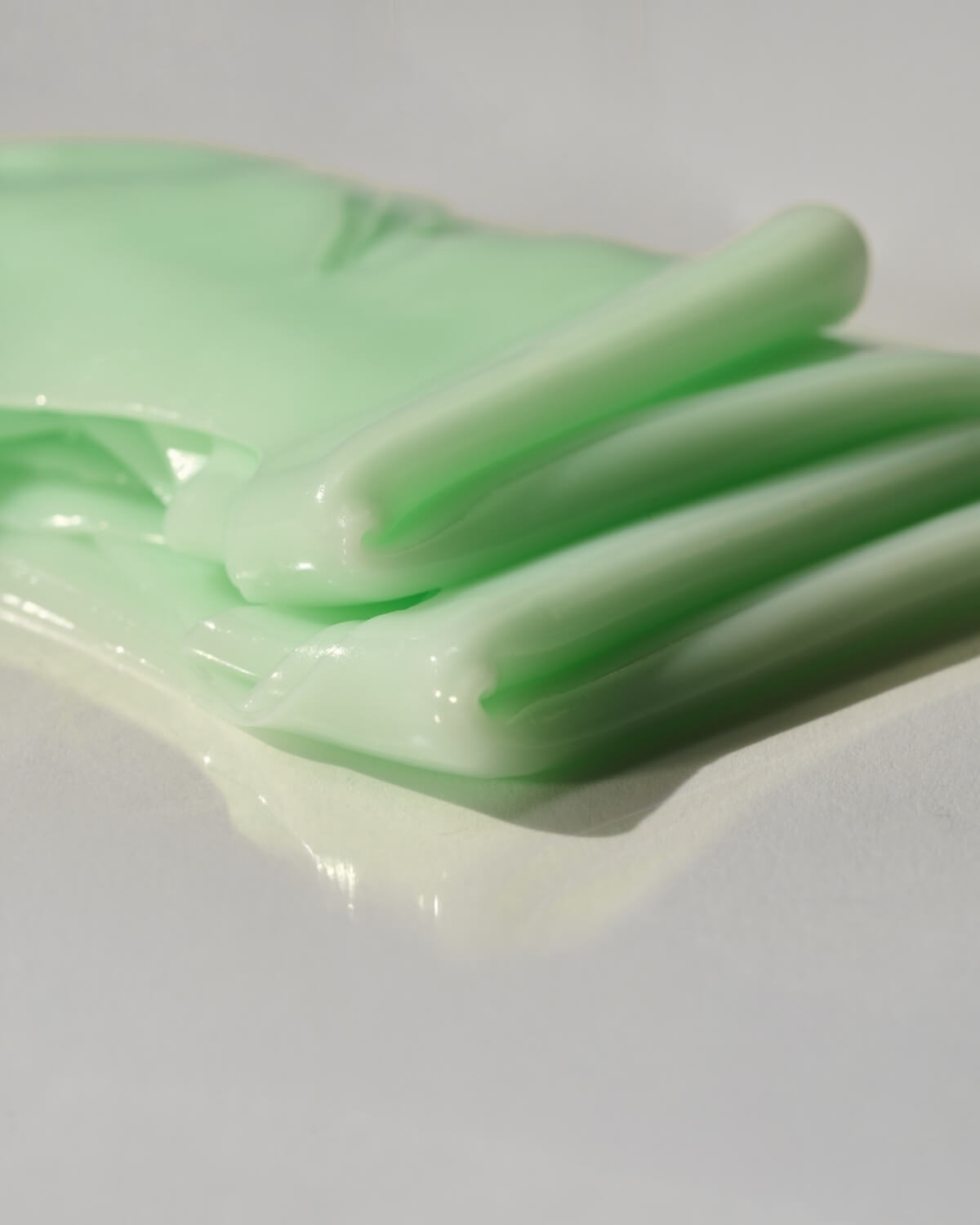 Detailed texture shot of a stacked, jelly-like pale green cooling hydrogel sheet mask on a clean white surface.