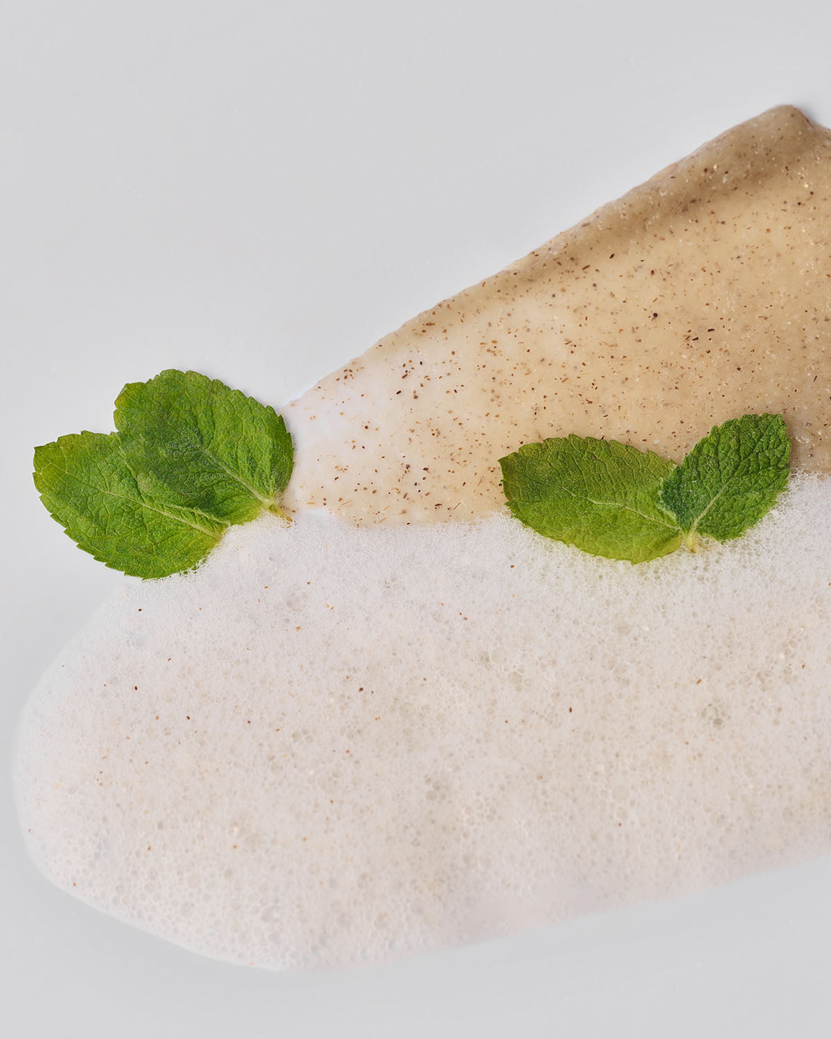 Green tea peeling cleanser gel texture with foaming lather and fresh mint leaves on a white background.