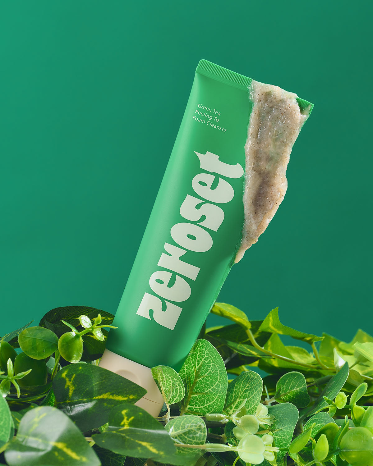 Zeroset green tea peeling cleanser tube with exfoliating gel swatch, resting on green foliage.