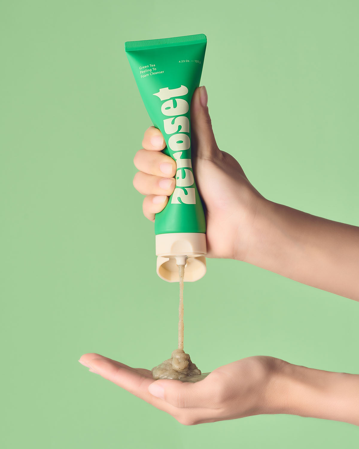 Person squeezing Zeroset green tea peeling to foam cleanser gel into open palm against green backdrop.