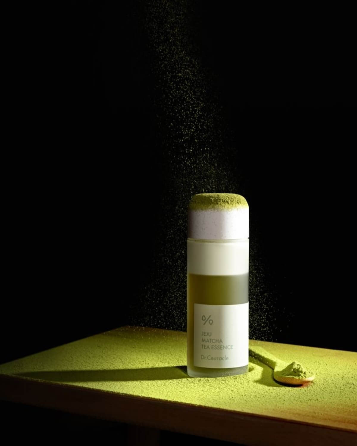 Dr. Ceuracle Jeju Matcha Tea Essence bottle with green matcha powder falling over it against a dark background.