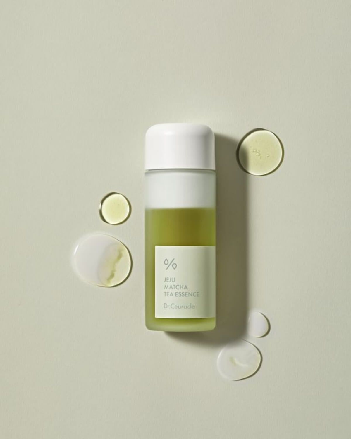 Flat lay of Dr. Ceuracle Matcha Essence bottle surrounded by translucent liquid droplets on a light green surface.