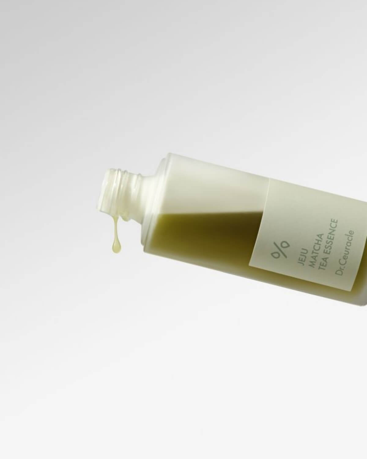 Close-up of a single drop of green tea essence dripping from the Dr. Ceuracle bottle opening.