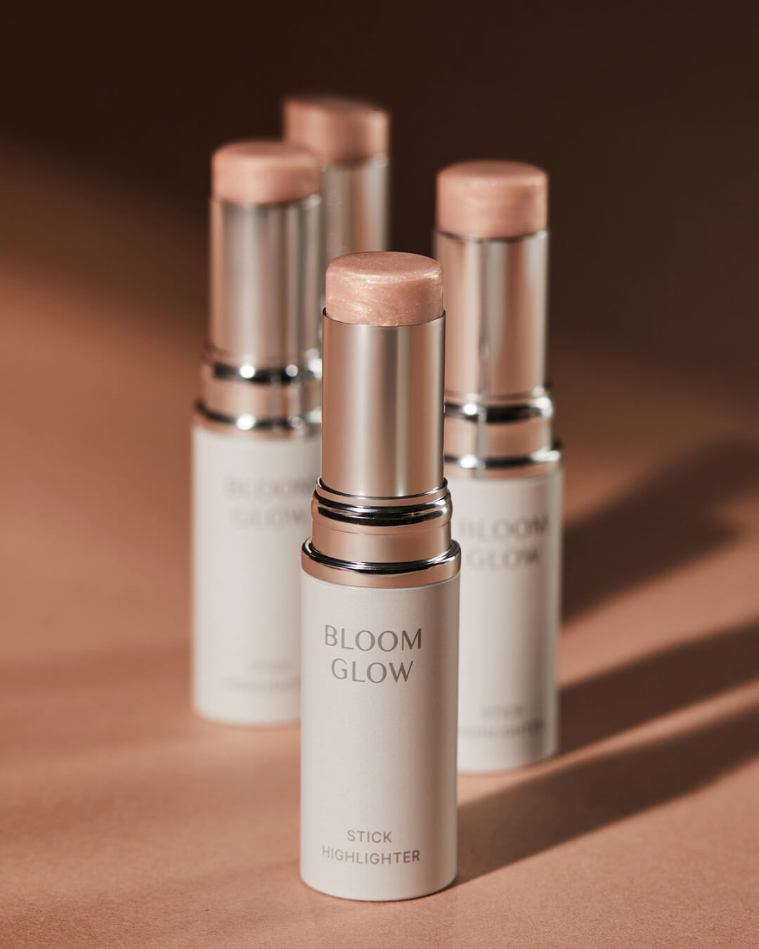 Four tubes of Koy Bloom Glow Stick Highlighter arranged on a warm tan surface with soft shadows.