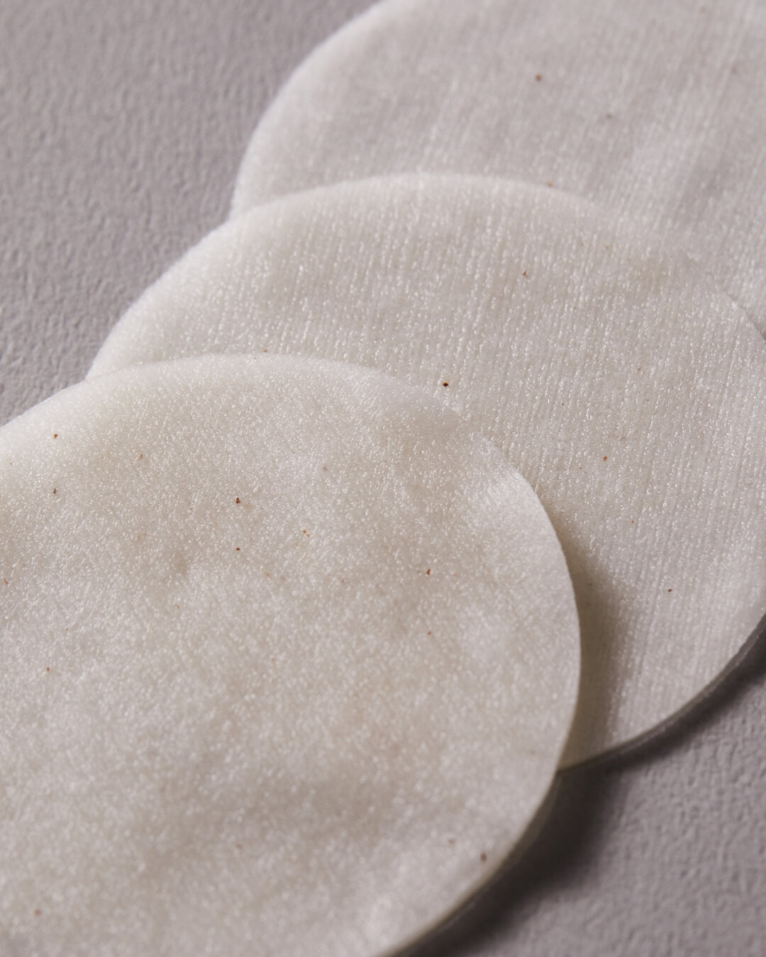 Close-up of three round white cotton pads from Koy Flow Soft Cotton Peel Pad on a textured surface.