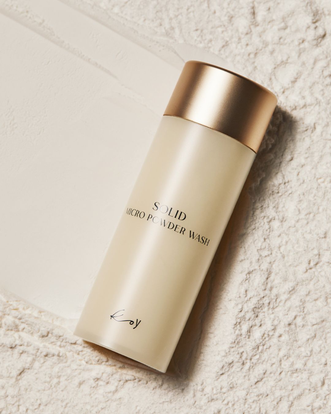 Koy Solid Micro Powder Wash bottle lying flat on a textured, powdery beige background showing product texture.