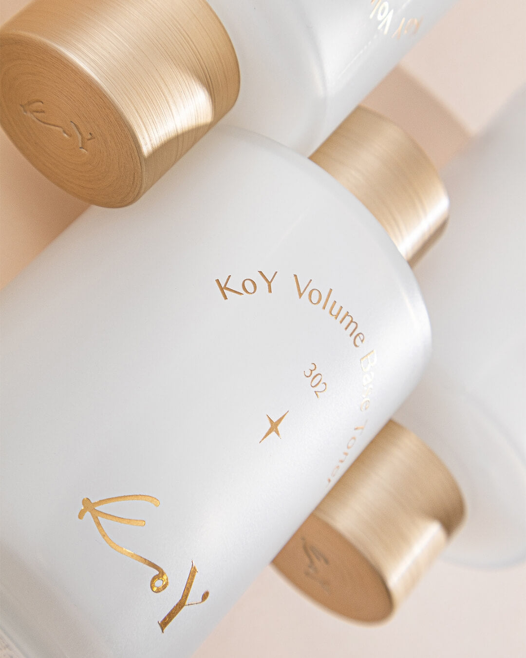 An overhead close-up view of three stacked KoY Volume Base Toner frosted glass bottles with gold caps.