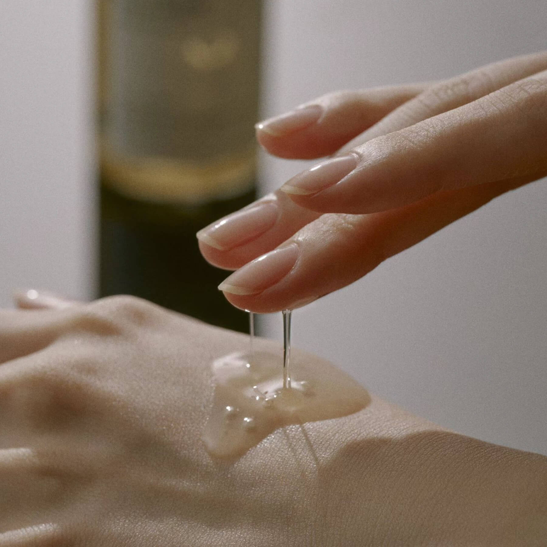 A close-up studio shot of the Mixsoon Bean Essence, showing its thick, honey-like texture dripping from one hand onto the back of the other, where a puddle of the essence is gathering, emphasizing its rich, hydrating quality.