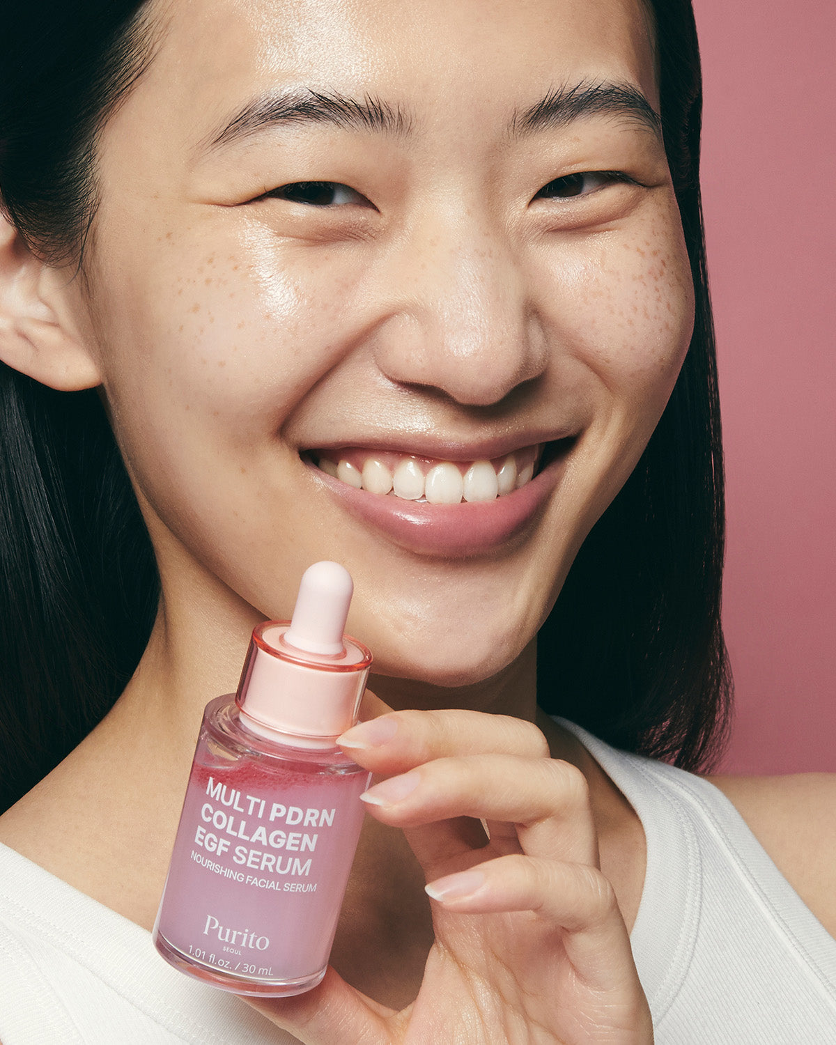 A woman smiling and holding a bottle of Purito Multi PDRN Collagen EGF Serum near her face.