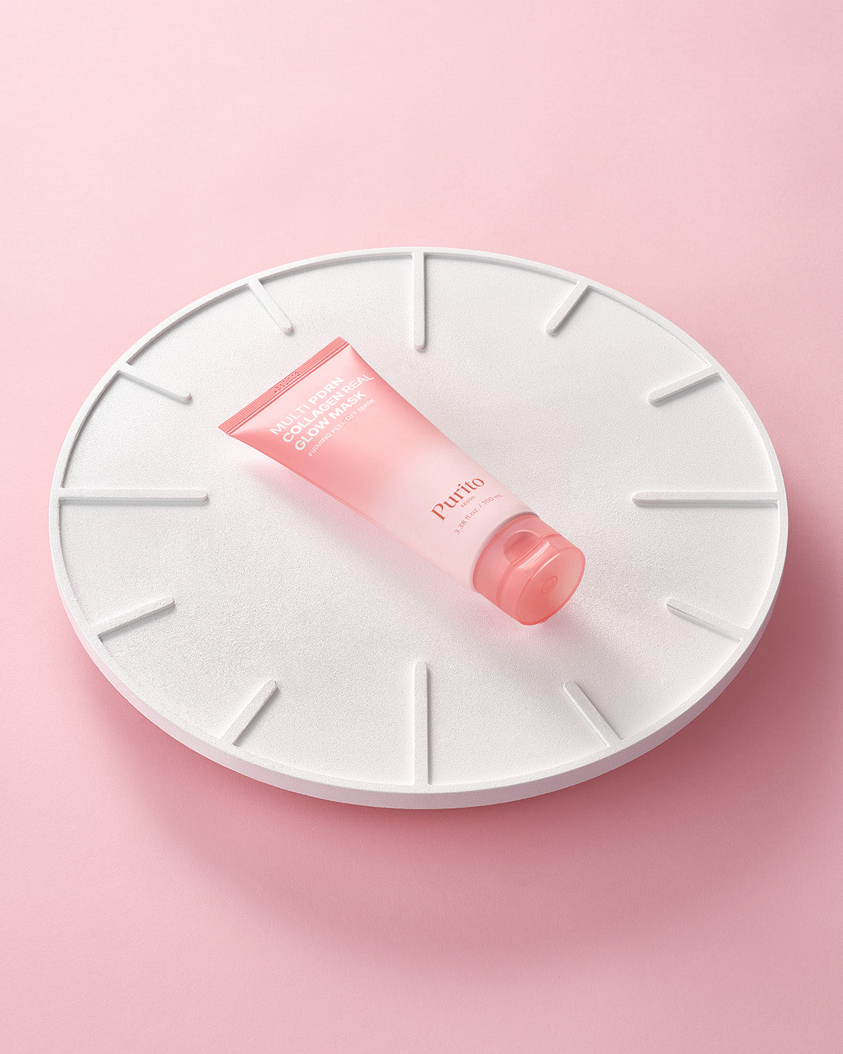 Purito Multi PDRN Collagen Real Glow Mask tube laying on a white circular textured pedestal.