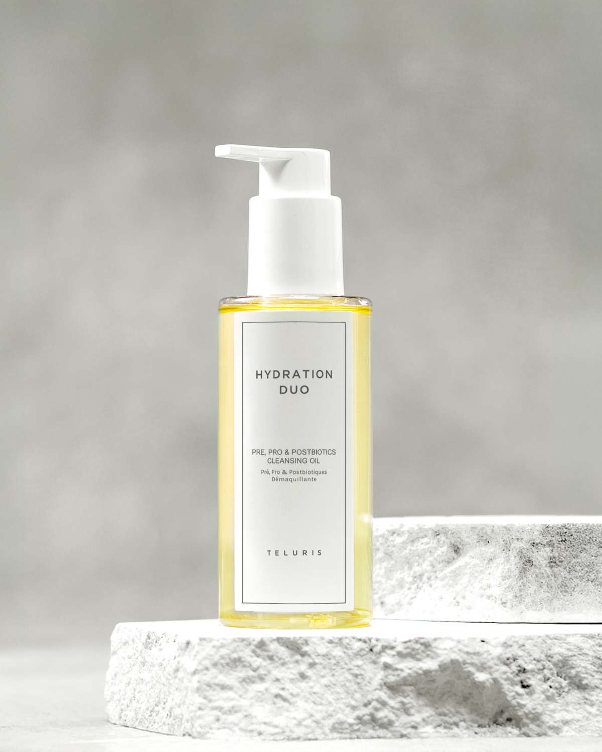 Yellow Teluris Cleansing Oil bottle displayed on a white stone pedestal with a grey background.