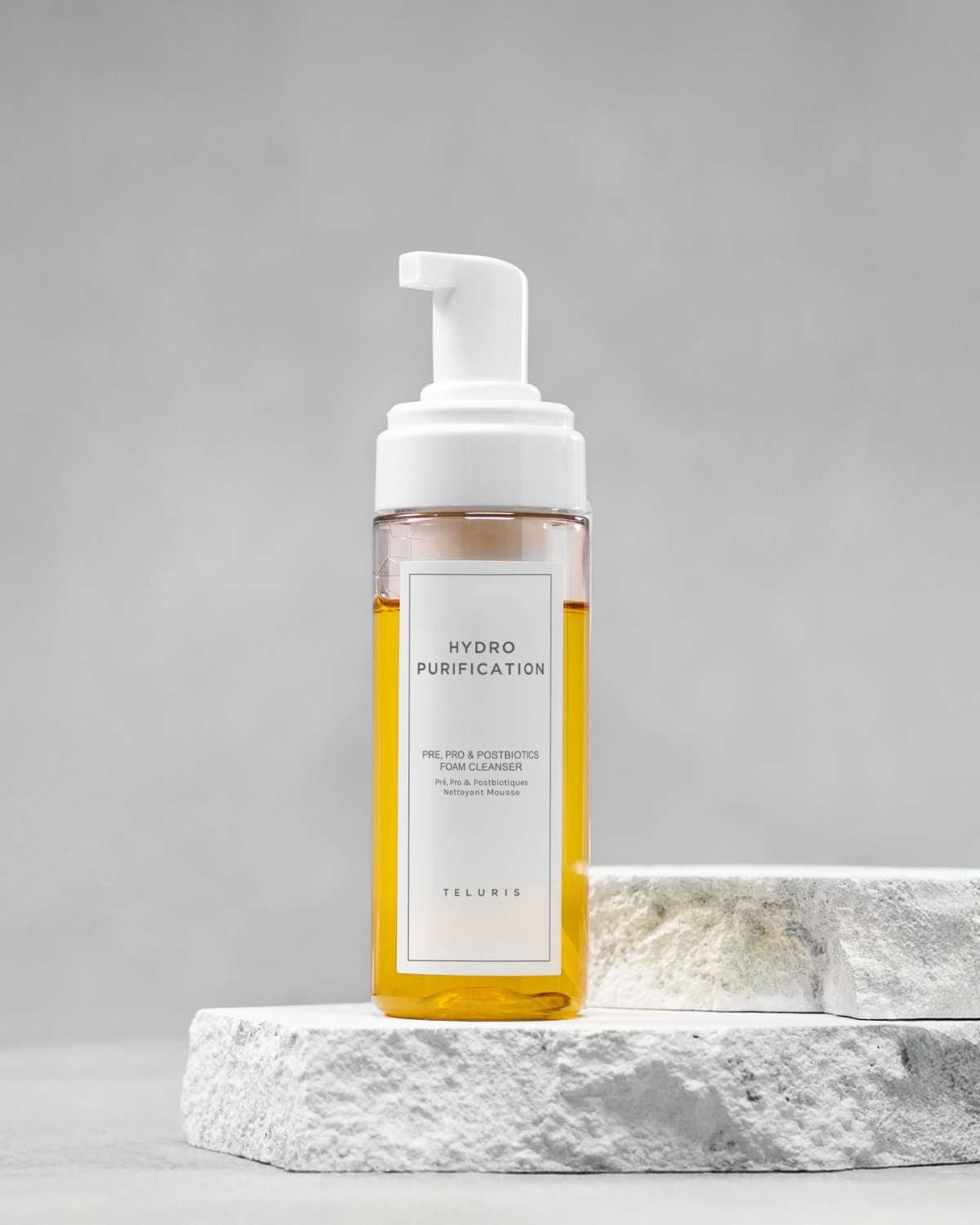 Teluris Hydro Purification foaming face wash on a stone pedestal with a clean grey background.