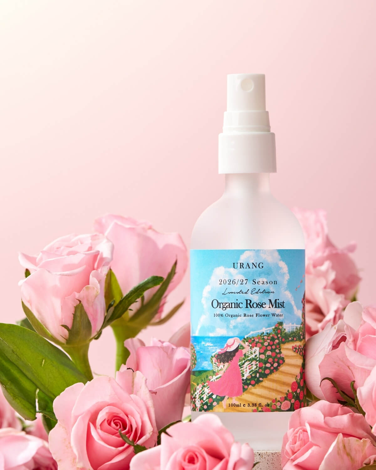URANG Organic Rose Mist bottle surrounded by fresh pink rose blossoms on a pastel pink background.