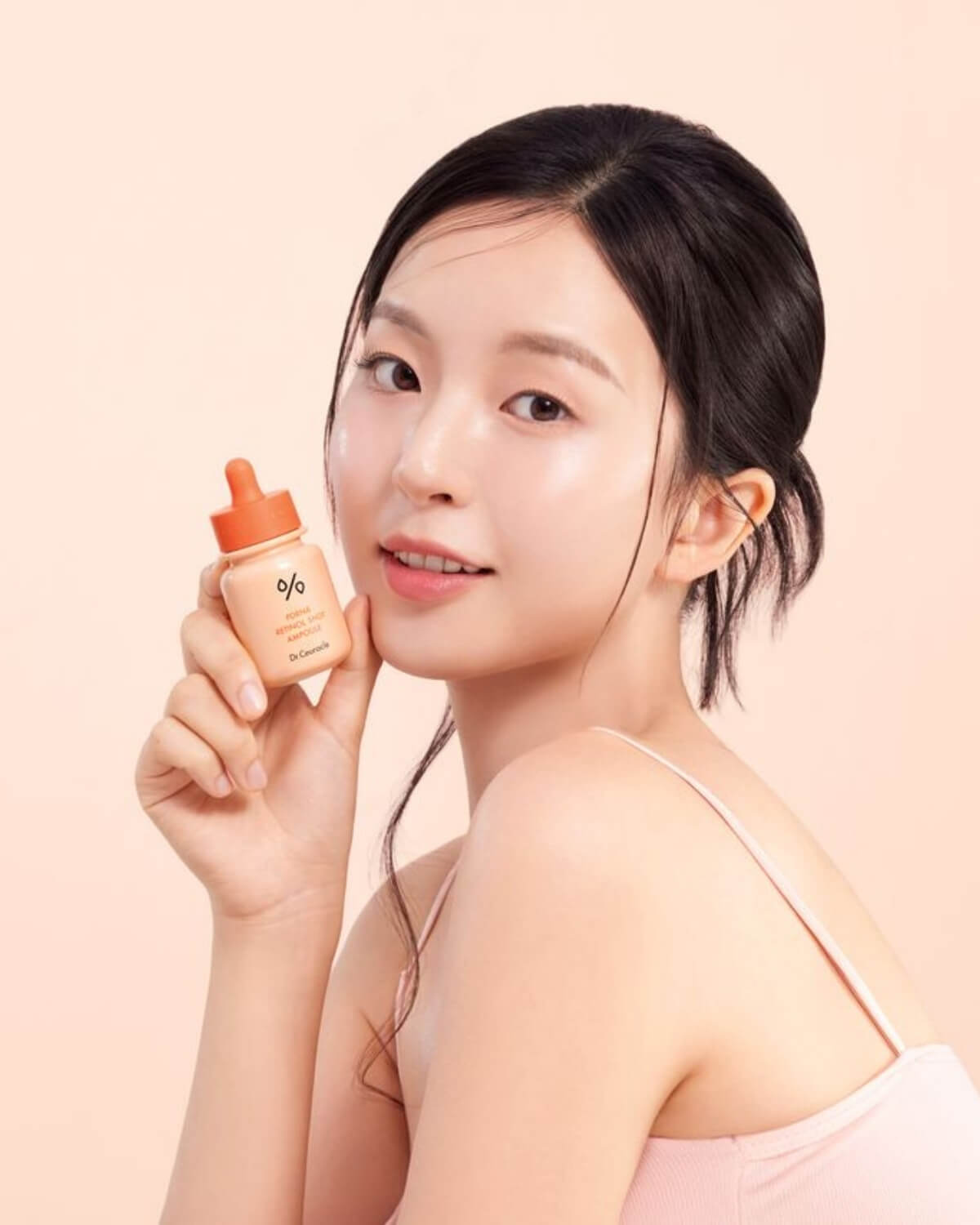 Model smiling while showcasing the Dr. Ceuracle PDRN & Retinol Shot Ampoule for clear, radiant skin.