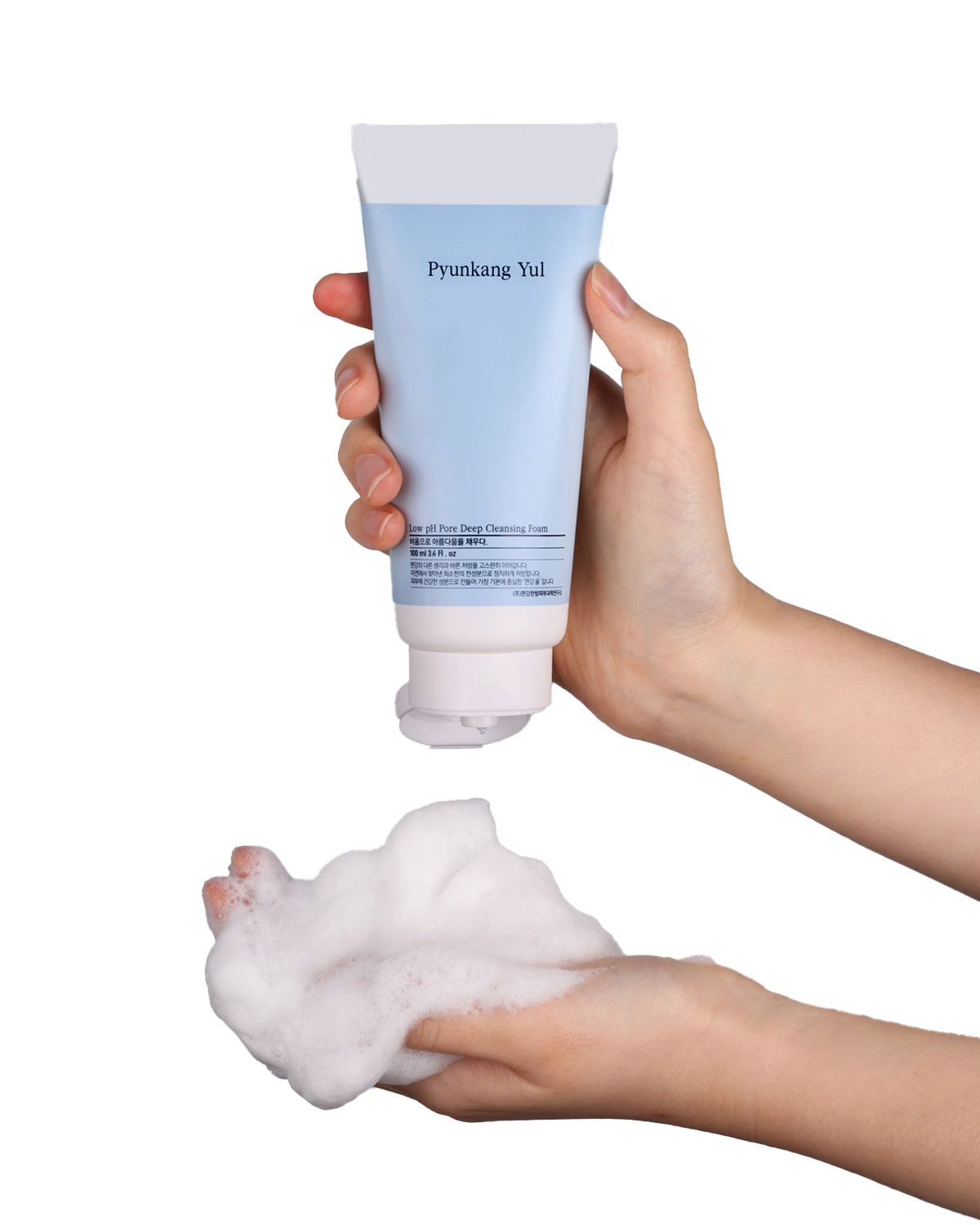 A light-skinned hand holds the light blue Pyunkang Yul Cleansing Foam tube, squeezing a line of white cream into a palm already filled with a cloud of rich, micro-foam lather, demonstrating the product's transformation.