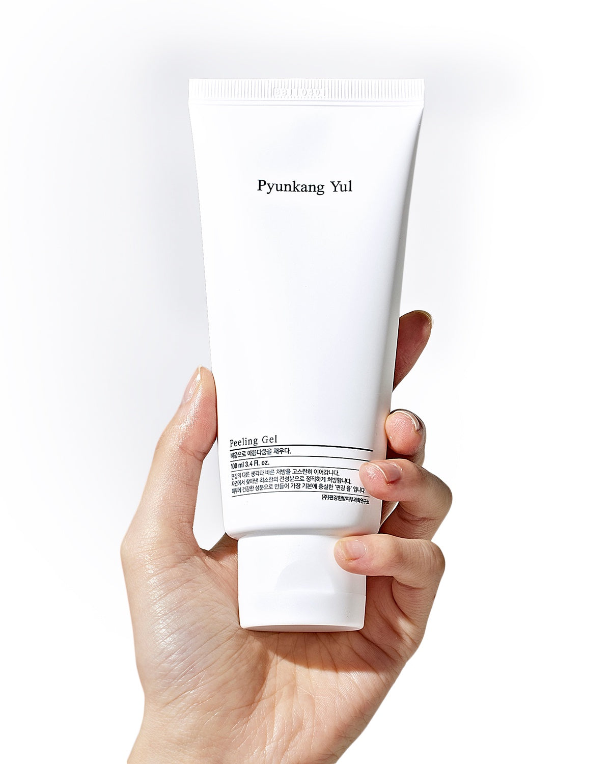 A light-skinned hand holds the upright white tube of Pyunkang Yul Peeling Gel, showcasing the simple label and white flip-cap, against a plain white background.