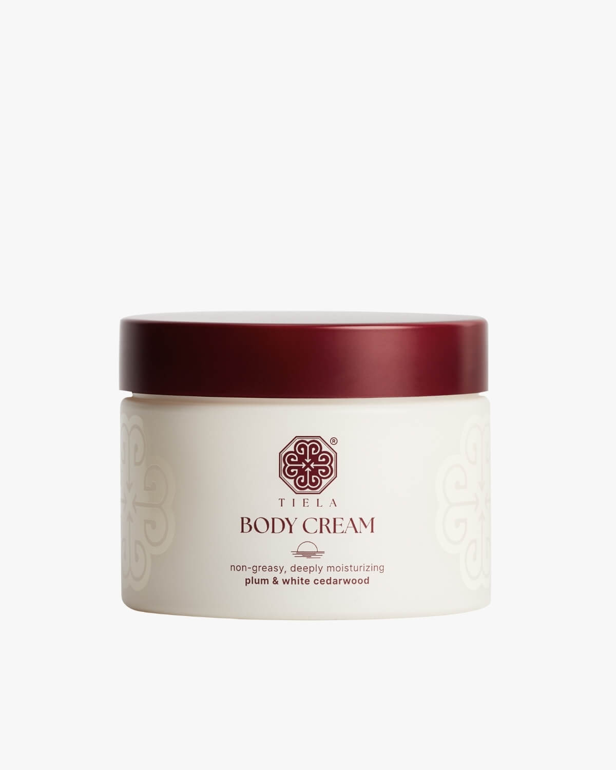 Front view of a round Tiela Body Cream jar with a deep red lid and white container, labeled "non-greasy, deeply moisturizing plum & white cedarwood."