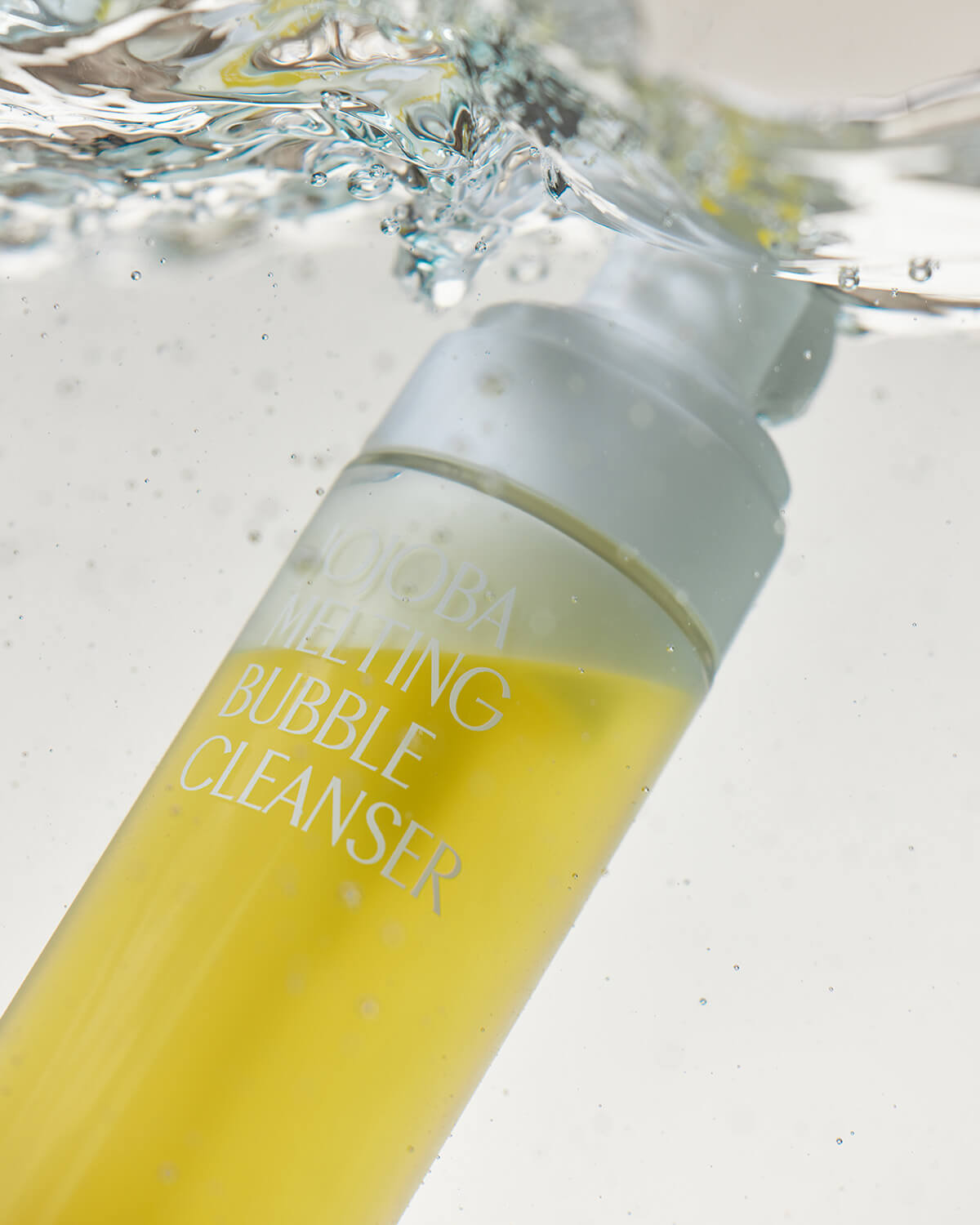 A dramatic underwater product shot of the Jojoba Melting Bubble Cleanser bottle submerged in clear water, with bubbles and turbulent splashing visible above the bottle's white pump cap.