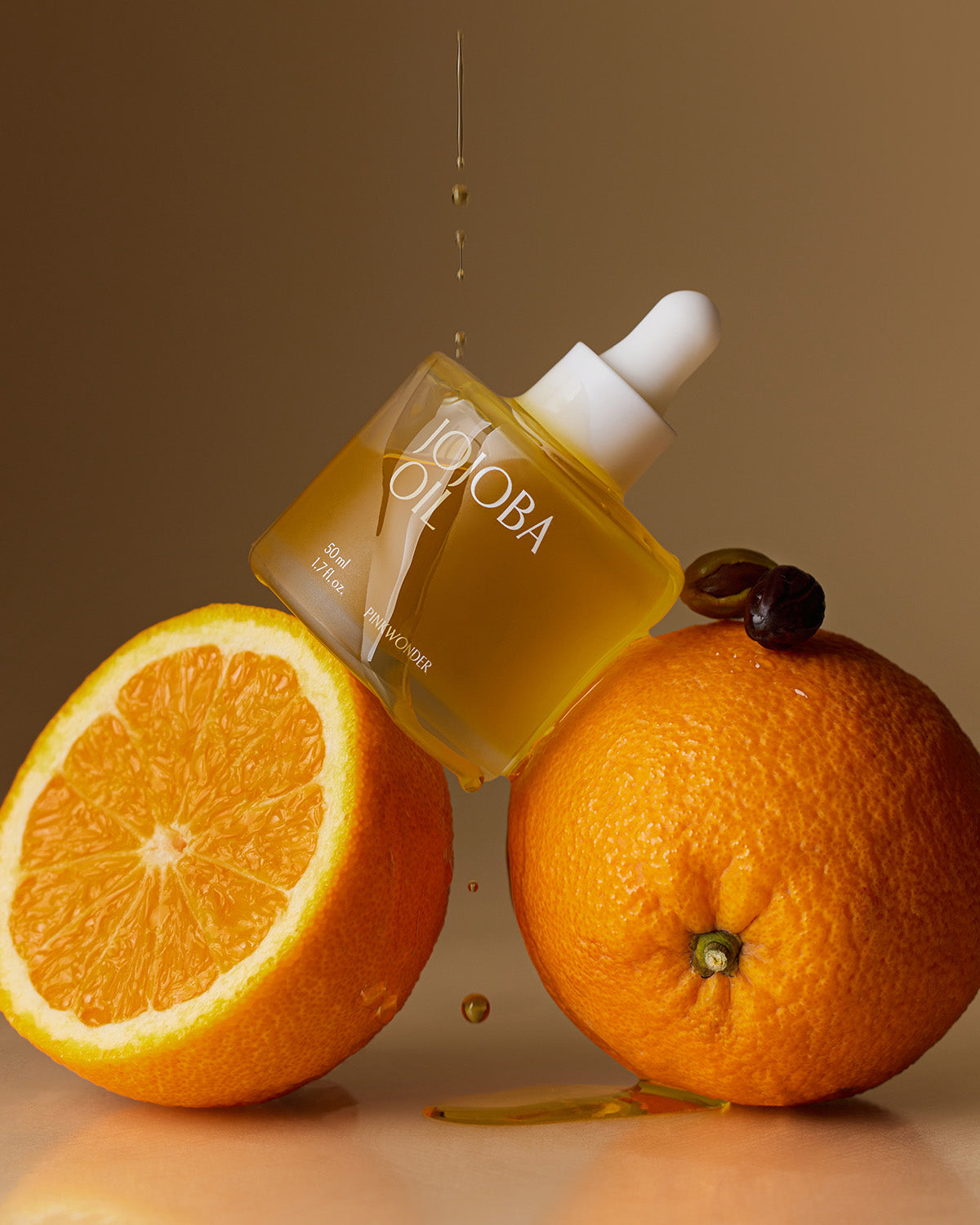 Pinkwonder Jojoba Oil bottle balanced on fresh oranges with golden oil drops, highlighting its natural and vitamin-rich formula.
