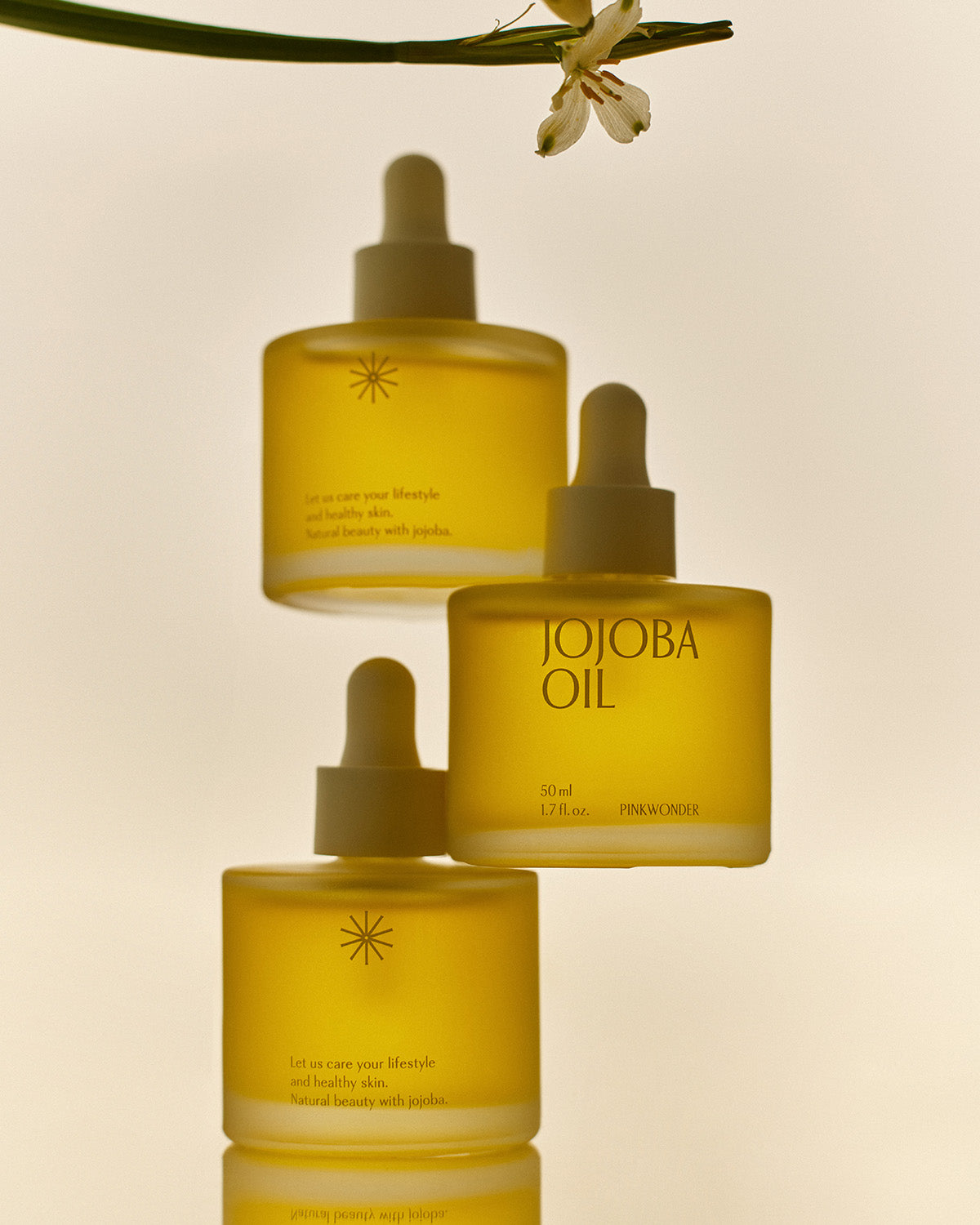 Three bottles of Pinkwonder Jojoba Oil arranged elegantly with soft lighting, showcasing the minimalist frosted glass packaging.