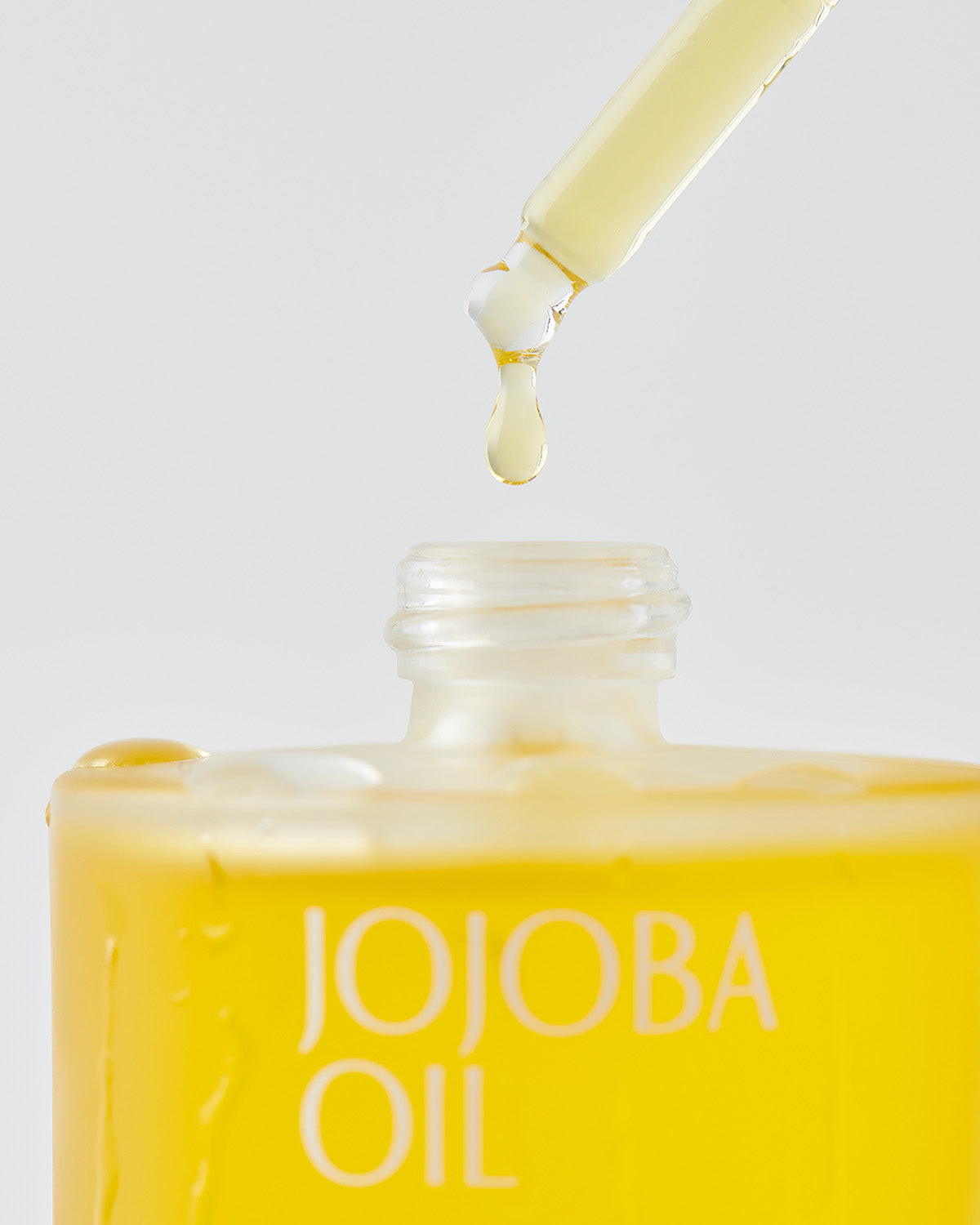 Close-up of Pinkwonder Jojoba Oil dropper releasing golden oil into the bottle, emphasizing purity and smooth texture.