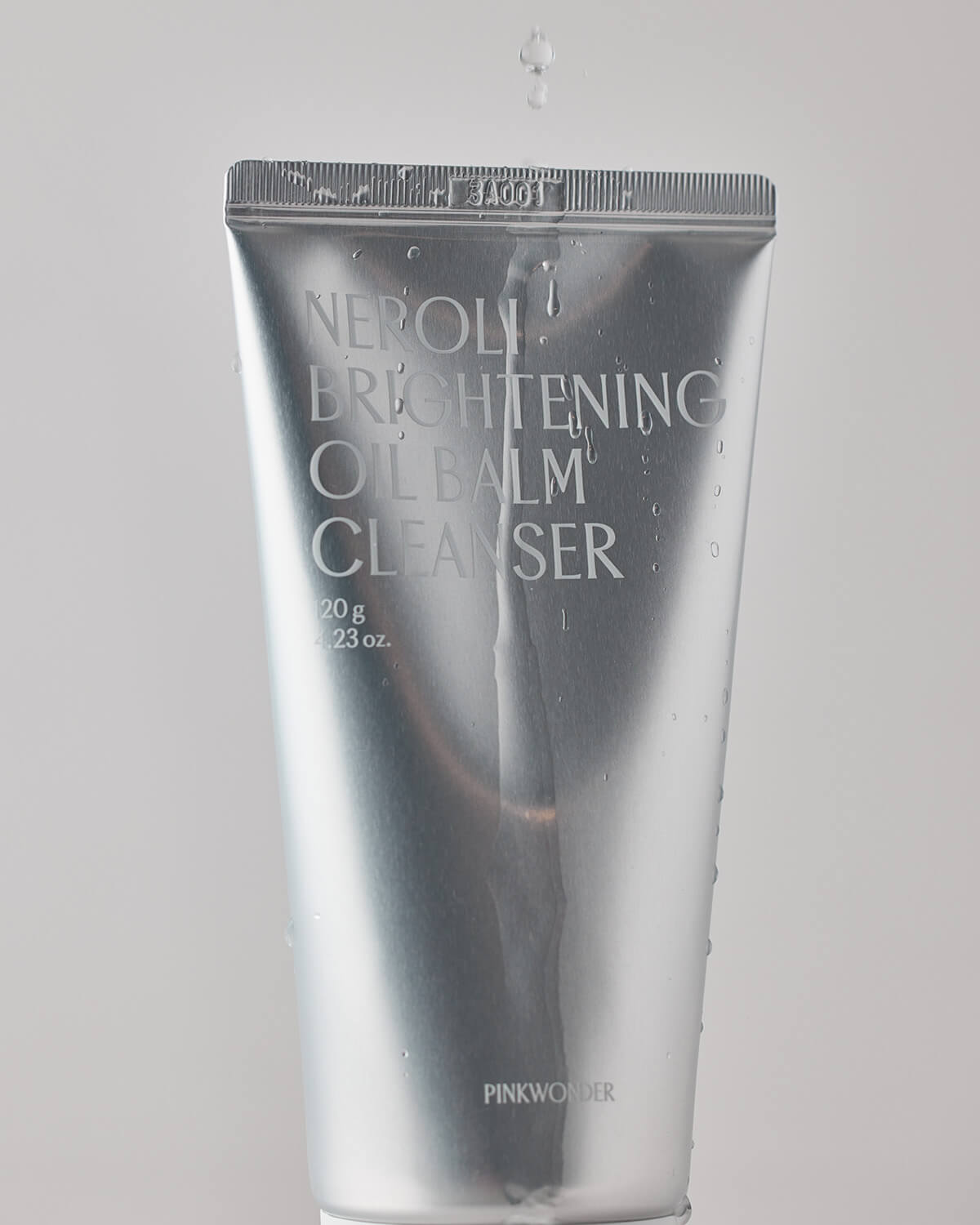 A dynamic close-up of the silver cleanser tube with water droplets on the surface, and a single drop of water falling onto the top crimped edge.