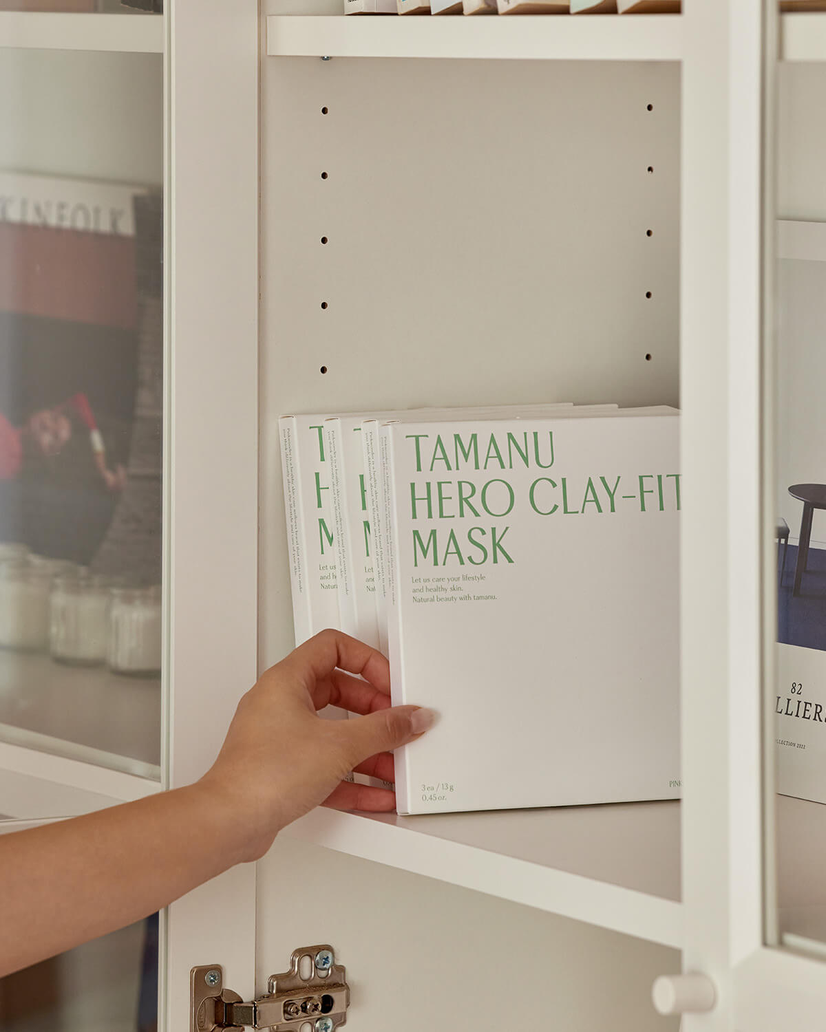 A close-up shot of a hand taking a white box of "Tamanu Hero Clay-Fit Mask" by Pinkwonder off a white shelf in a closet.