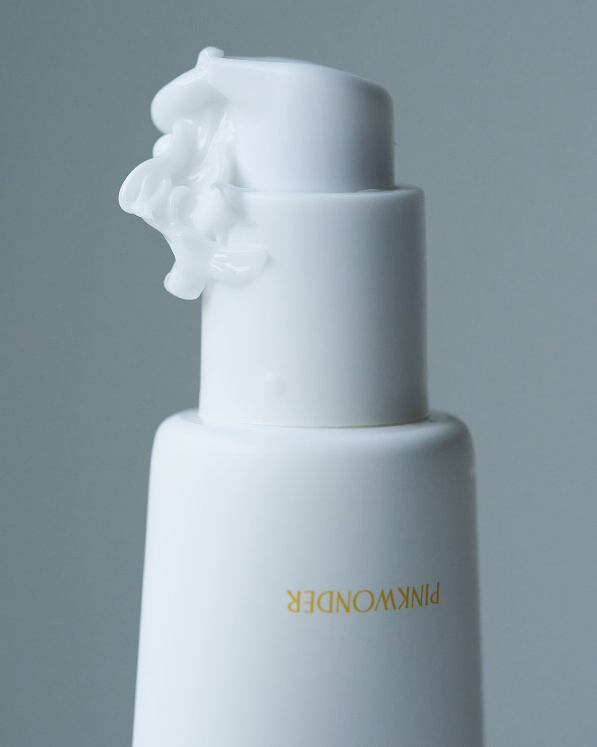 An extreme close-up of the pump dispenser on the Pinkwonder Jojoba Barrier Plus Cream. A small amount of the white cream is visible, having been dispensed and curling around the nozzle.