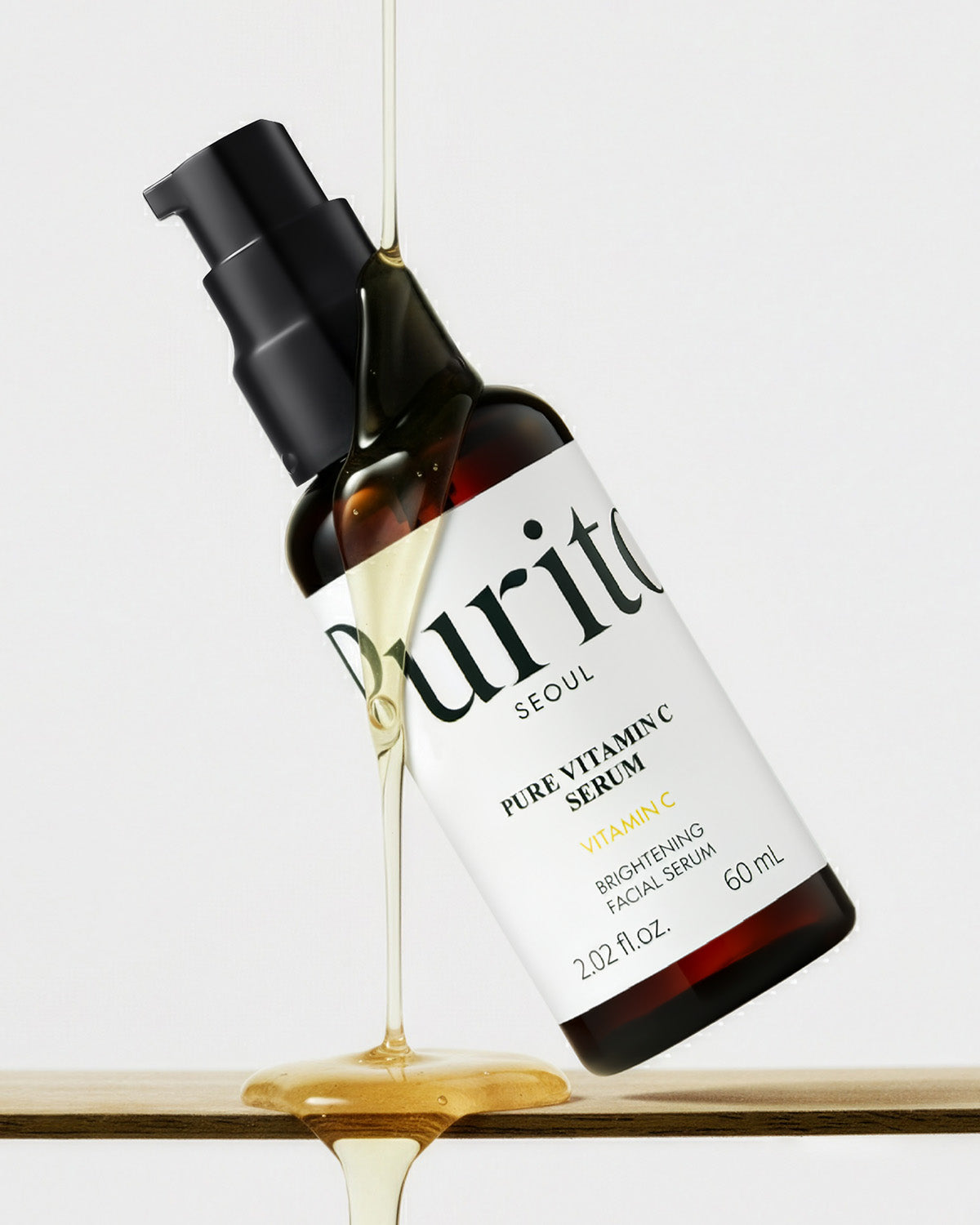 Purito Pure Vitamin C Serum bottle tilted with a thick golden liquid serum pouring over it.