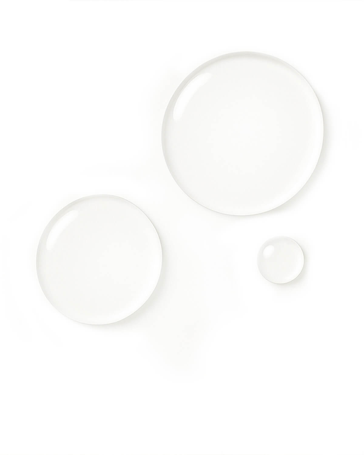 Close-up macro shot of three distinct, clear, circular drops of the serum product on a white surface, showcasing its transparent texture.