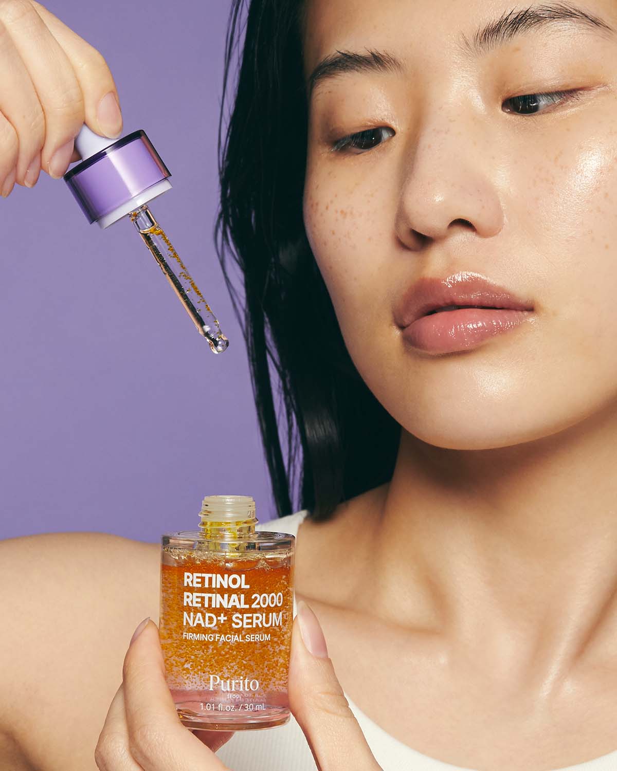 Model holding a dropper above the Purito Retinol Retinal 2000 NAD+ Serum bottle.