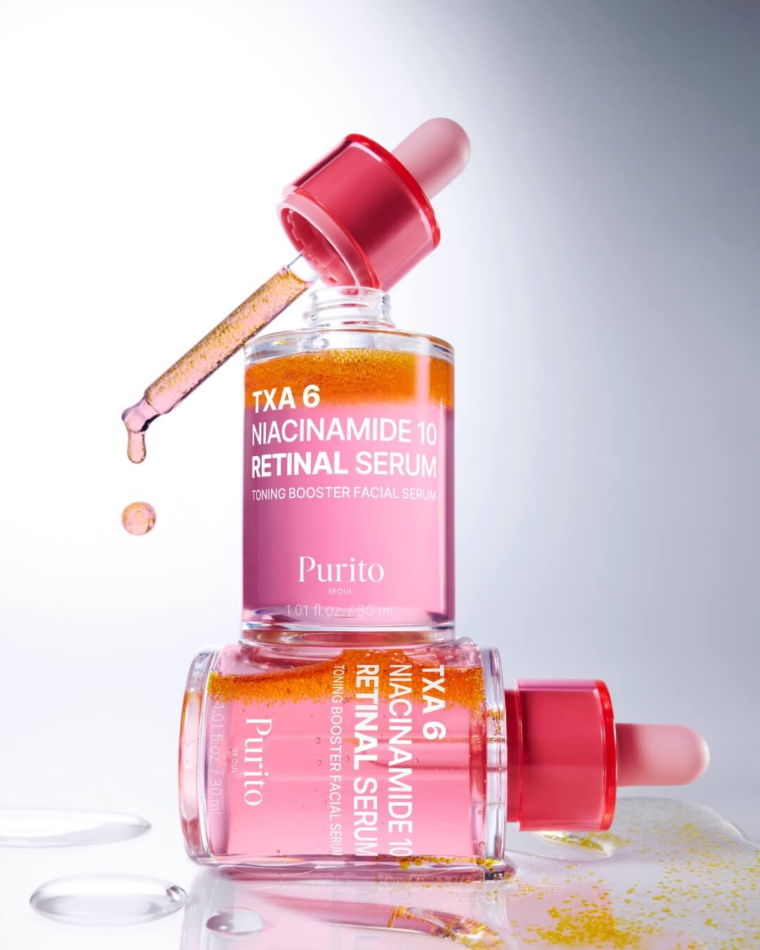 A dynamic studio shot featuring two bottles of Purito TXA 6 Niacinamide 10 Retinal Serum stacked on top of each other. The top bottle's pink dropper is pulled out, with a drop of the yellow-orange serum dripping from the tip. The bi-phase pink and orange serum is clearly visible in both bottles.