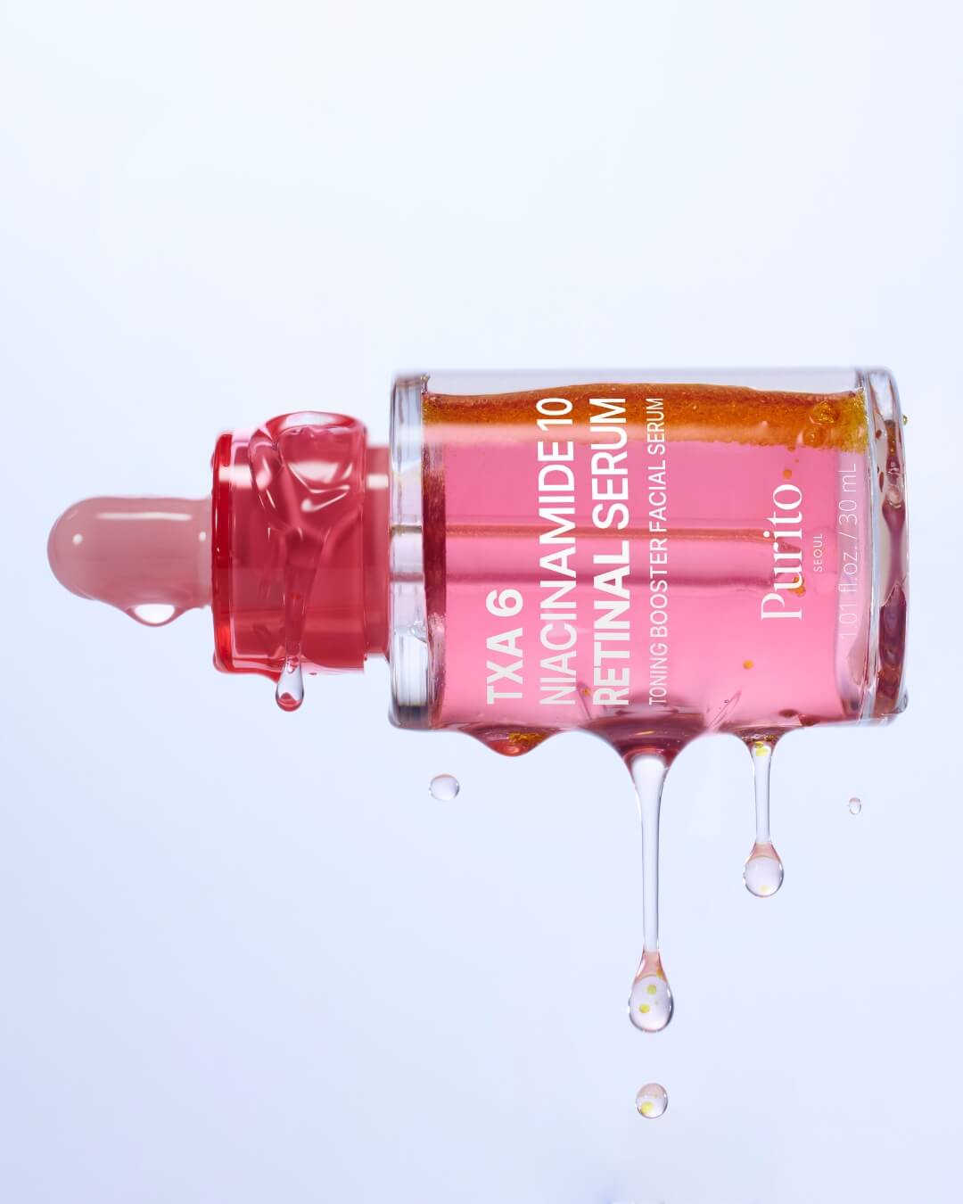 A macro studio shot of the Purito TXA 6 Niacinamide 10 Retinal Serum bottle lying on its side. The bi-phase liquid is spilling out and dripping down, highlighting the vivid orange and pink colors of the serum.